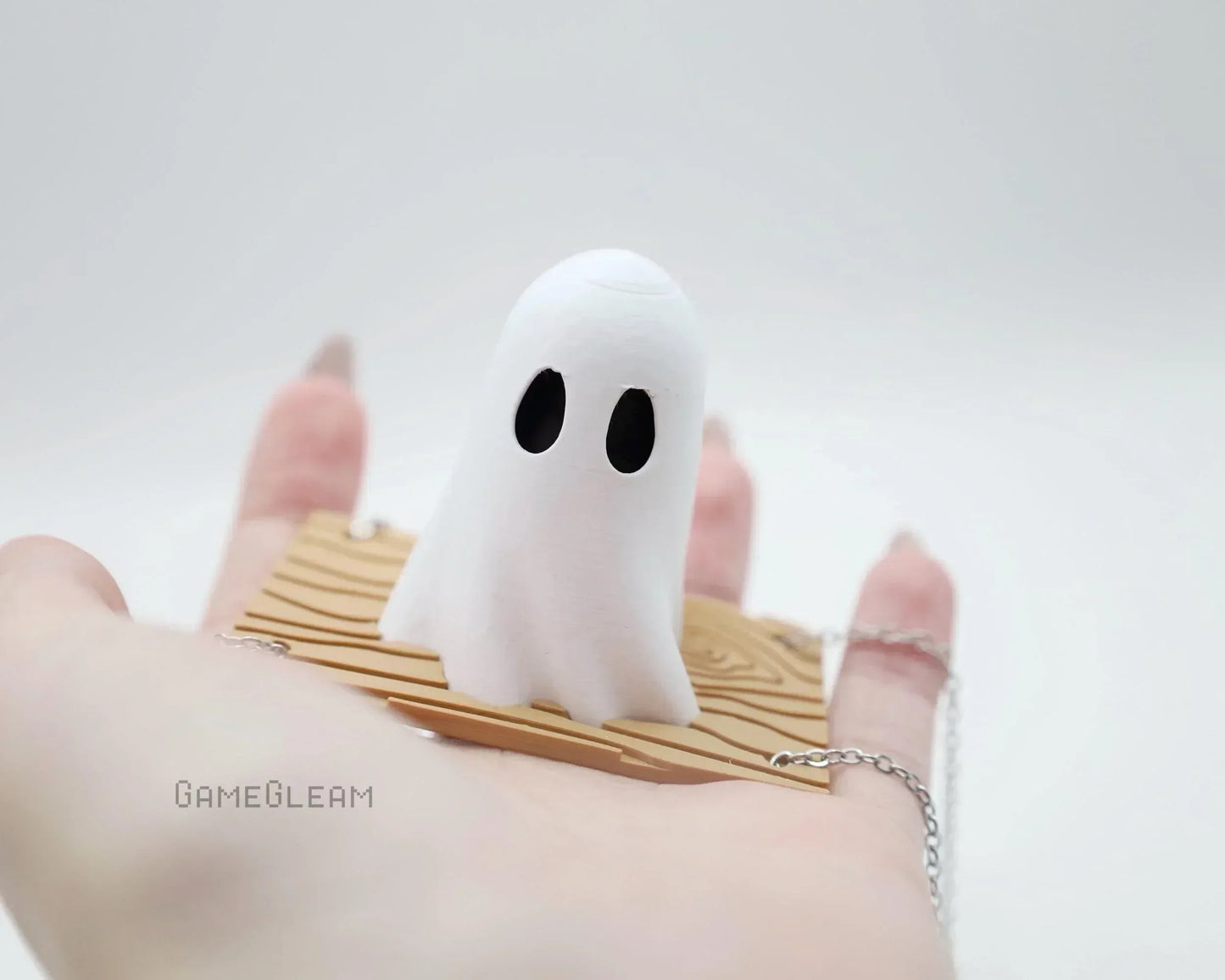 Hand holding a cute ghost figurine on a wooden plank with silver chain, minimal background