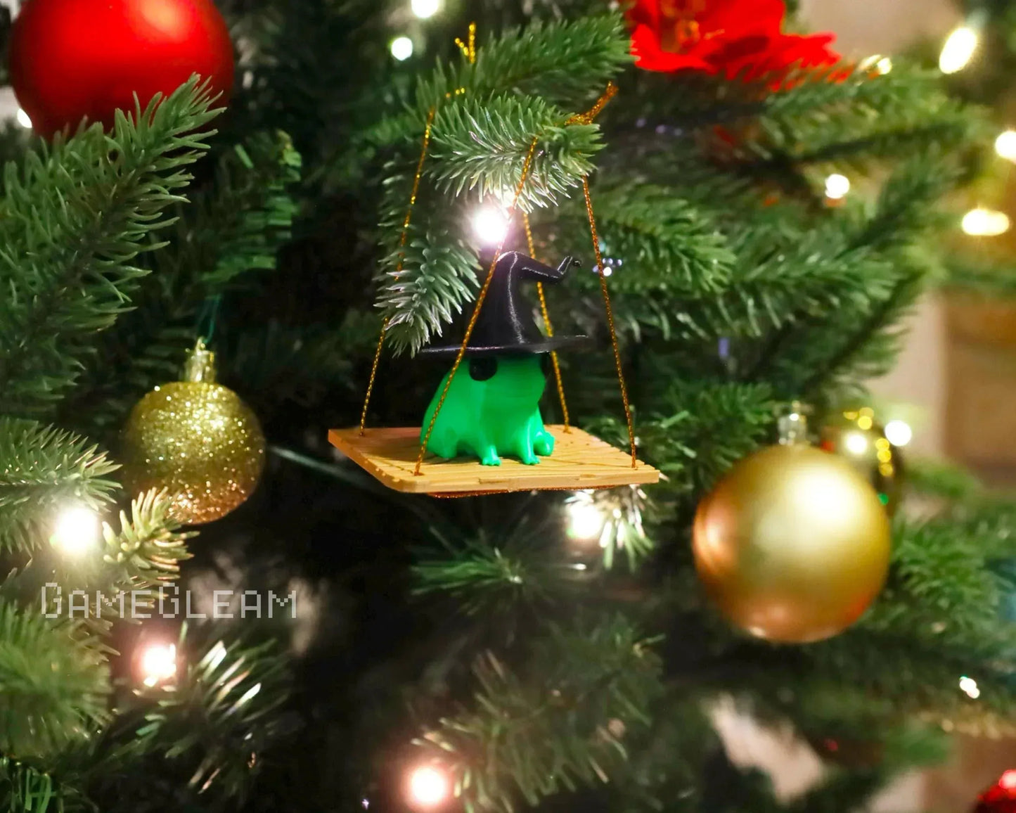 Handmade Christmas tree ornament of a green frog with a wizard hat on a swing, surrounded by festive baubles and holiday lights.