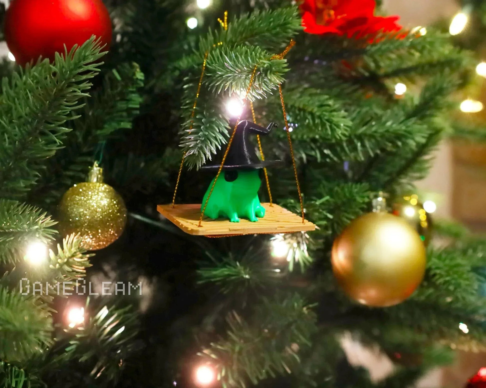 Handmade Christmas tree ornament of a green frog with a wizard hat on a swing, surrounded by festive baubles and holiday lights.