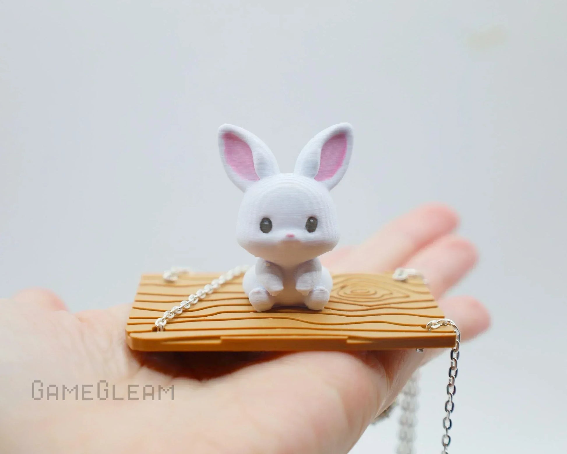 Cute white bunny figurine on wood-textured platform with silver chain, held in hand