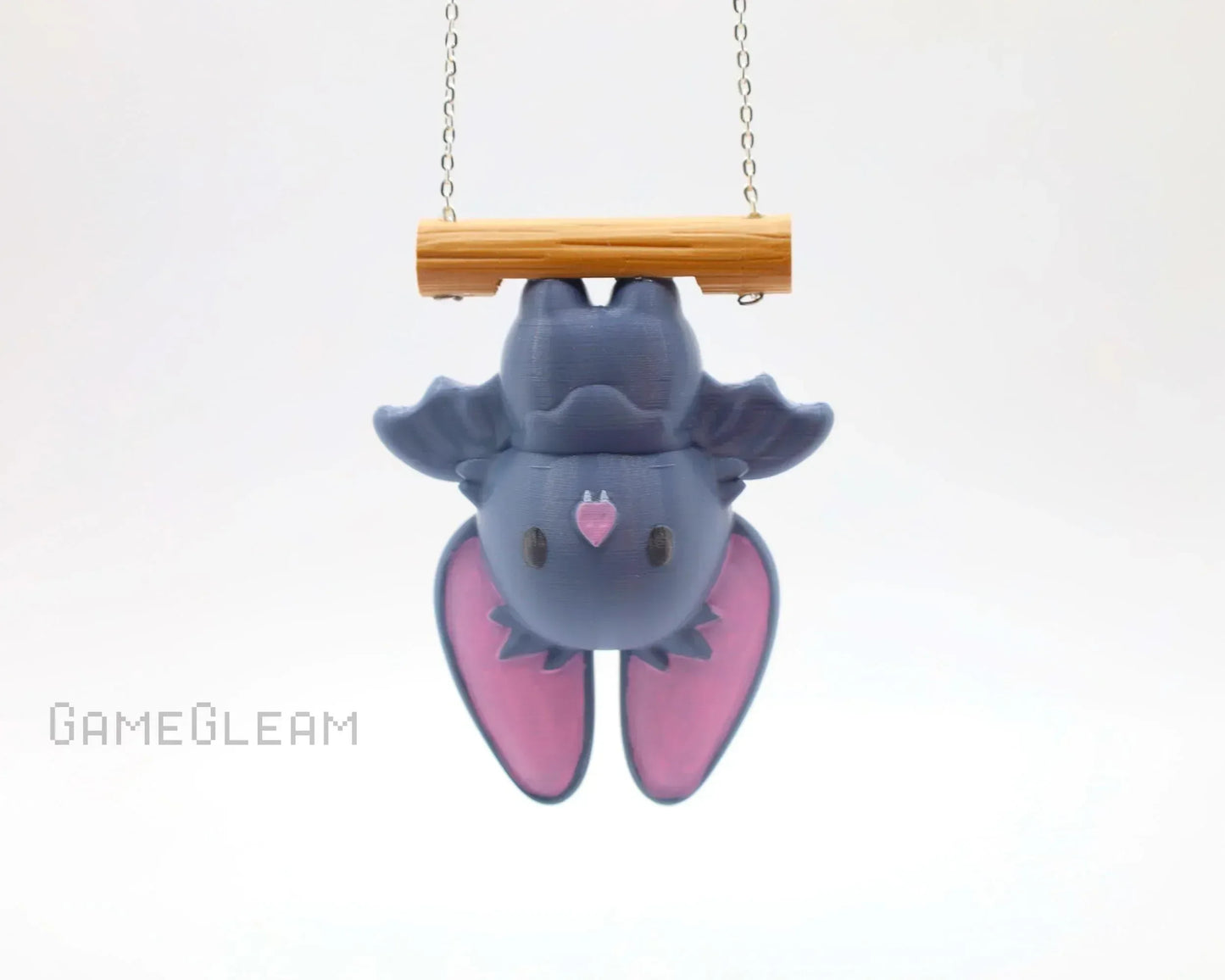 Cute handmade bat charm with pink wings hanging upside down from a wooden perch