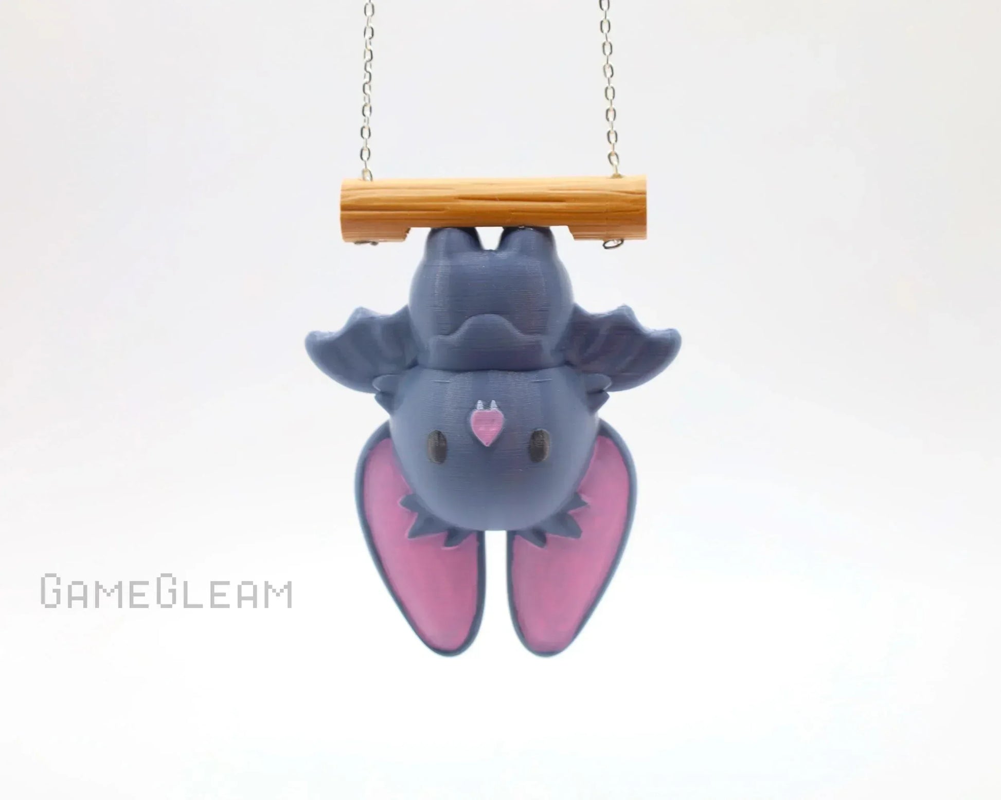 Cute handmade bat charm with pink wings hanging upside down from a wooden perch