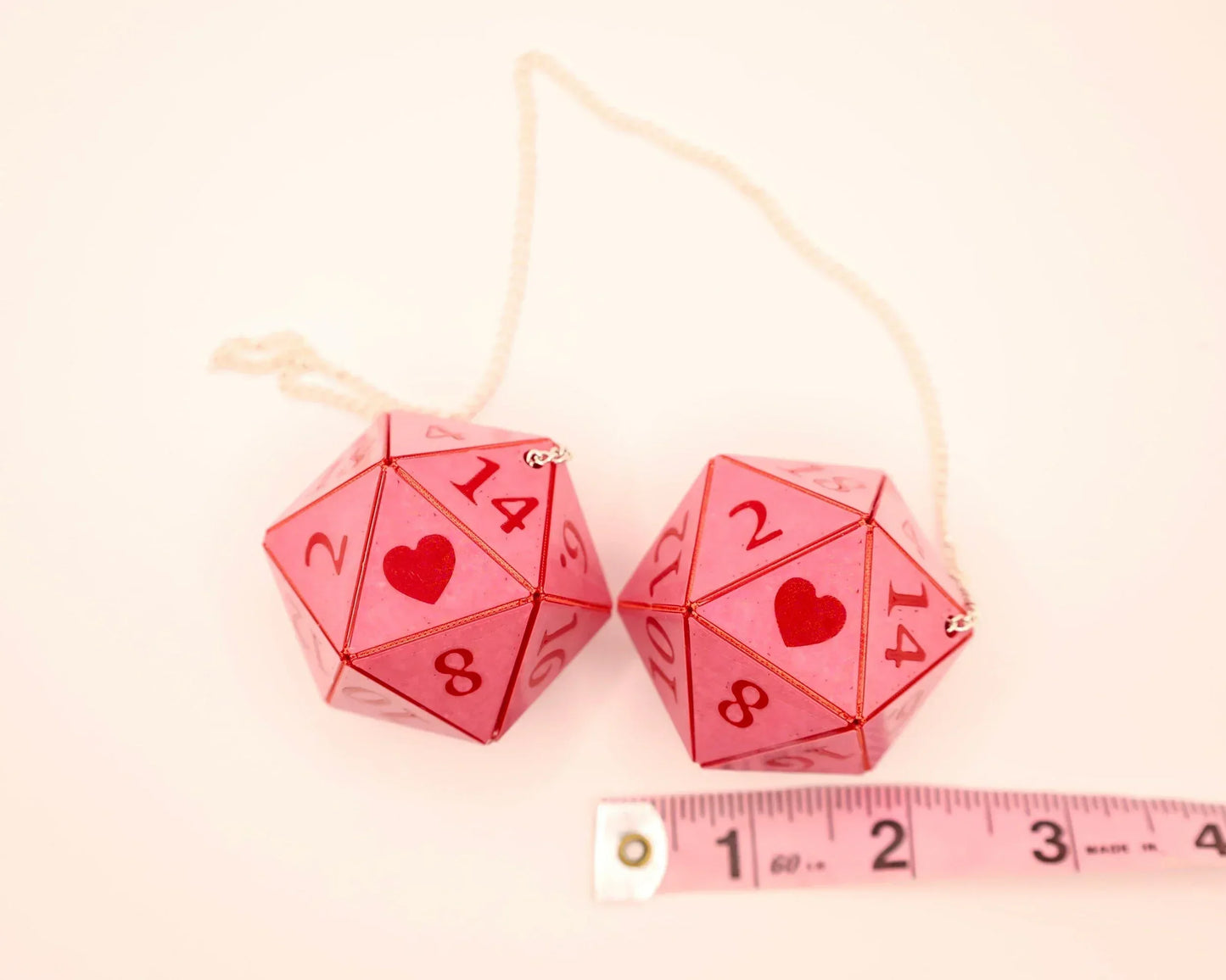 Pink twenty-sided car dice charms with red hearts, chain, and measuring tape for size reference