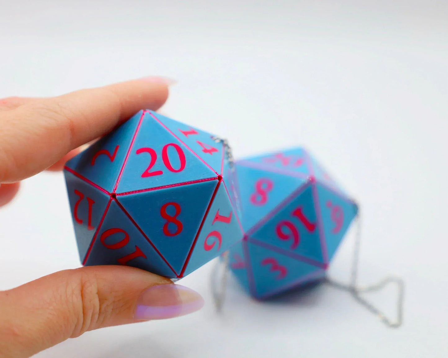 Blue twenty-sided dice with pink numbers, held by a hand, attached to a silver chain.