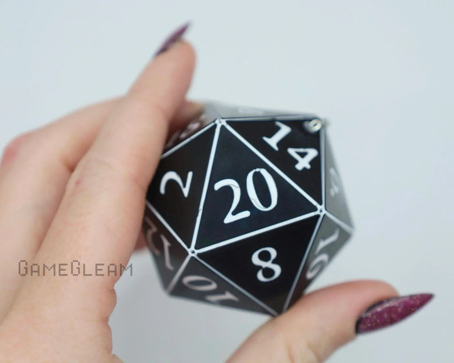 Hand holding a black 20-sided dice with white numbers, perfect for tabletop gaming fans.