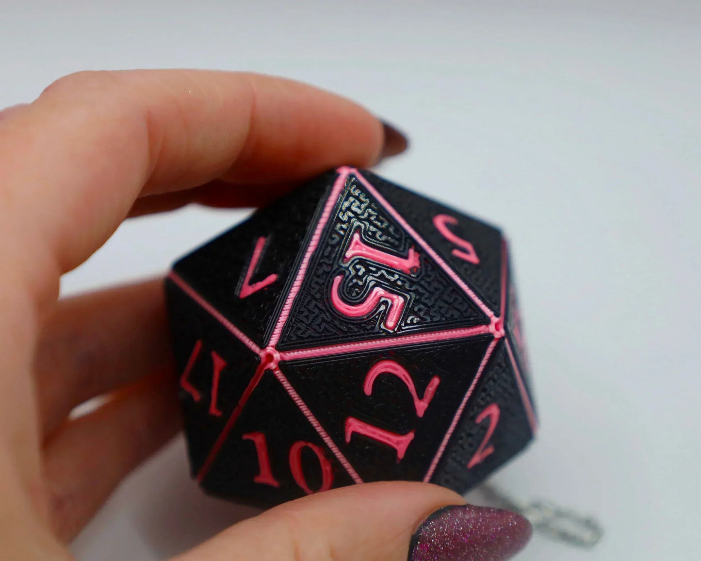 Hand holding a black and pink twenty-sided RPG dice charm, textured design, close-up