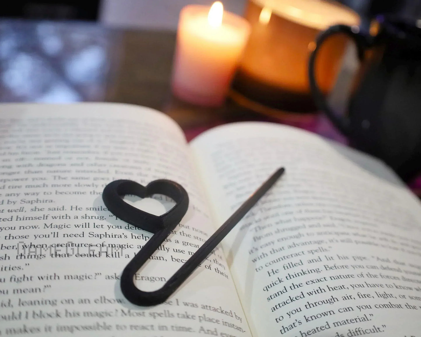 Heart-shaped black page holder on open book with lit candle and mug in cozy reading setting
