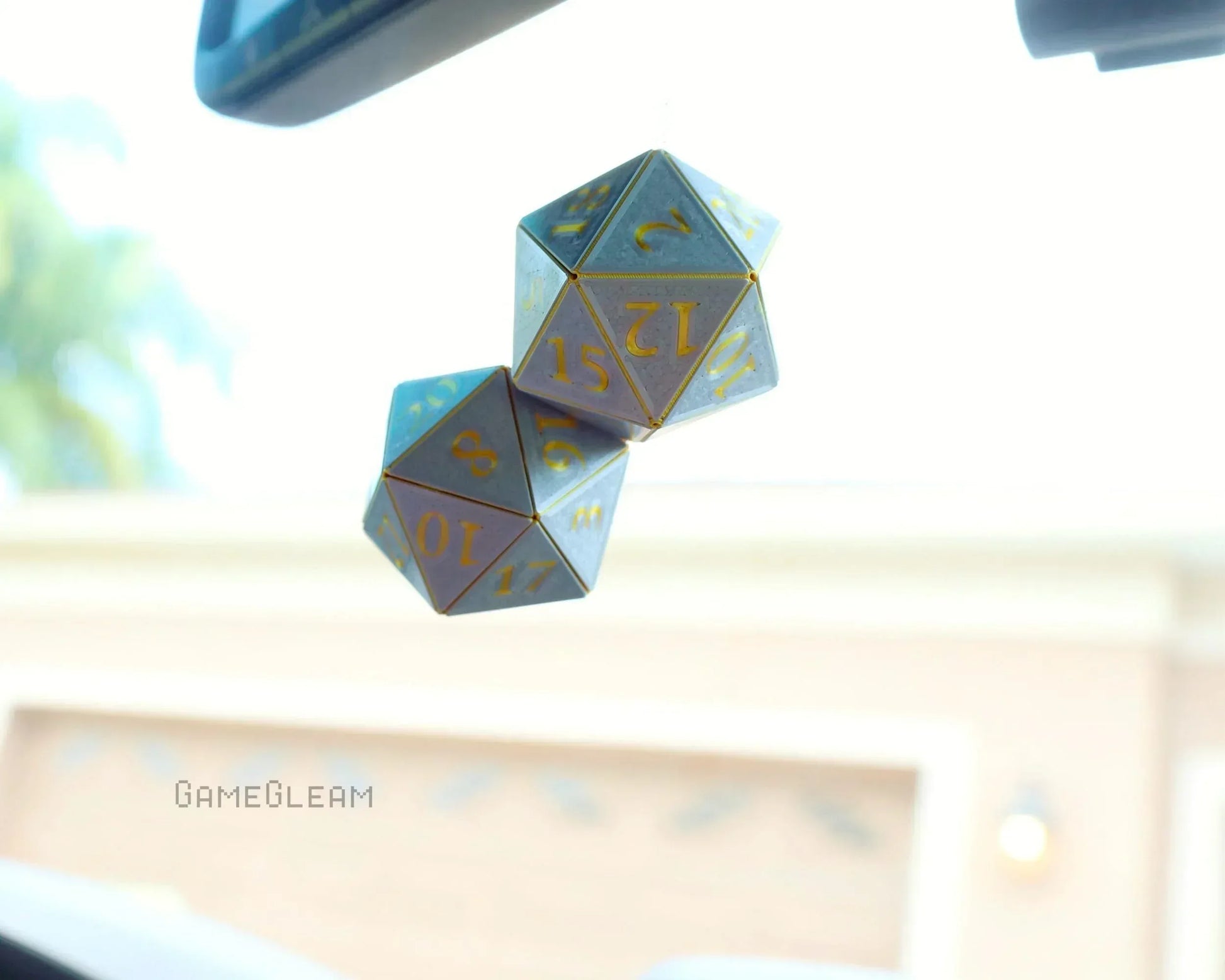 Holographic twenty-sided dice car charm with gold numbers hanging from rearview mirror