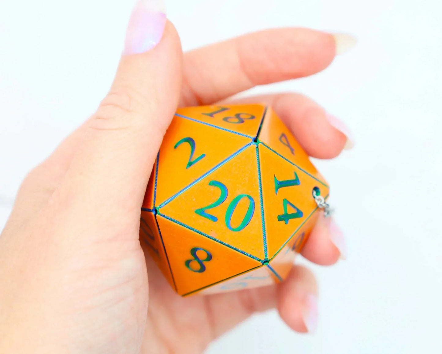 Hand holding a large orange twenty-sided dice with blue numbers, car charm accessory