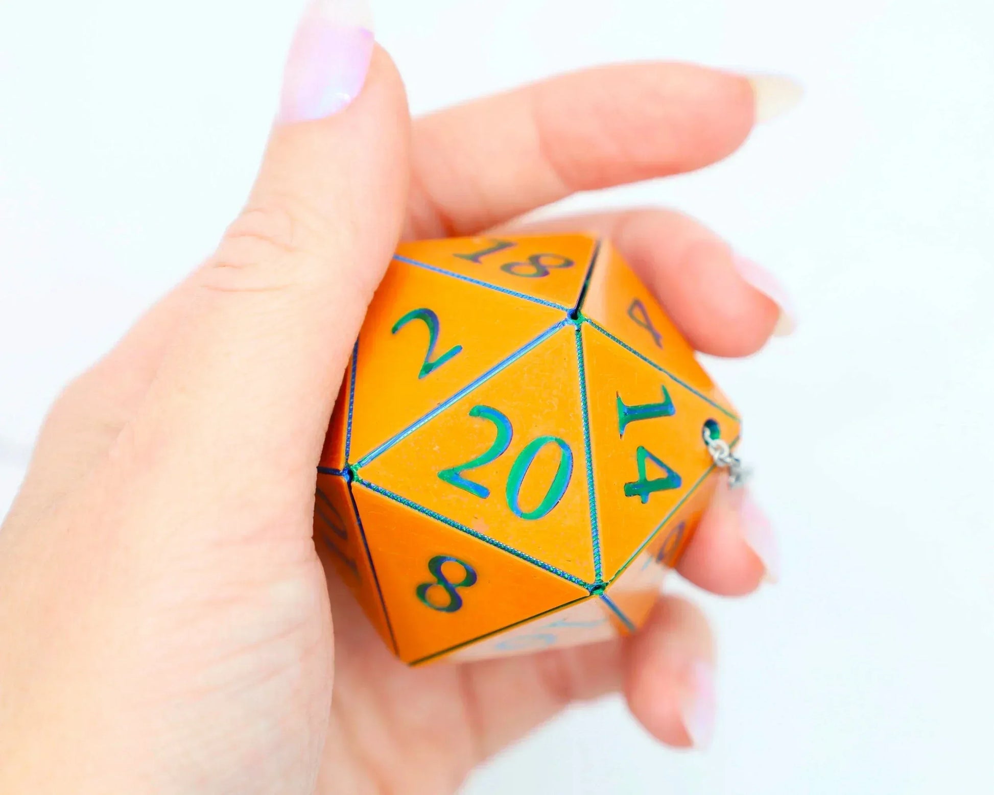 Hand holding a large orange twenty-sided dice with blue numbers, car charm accessory