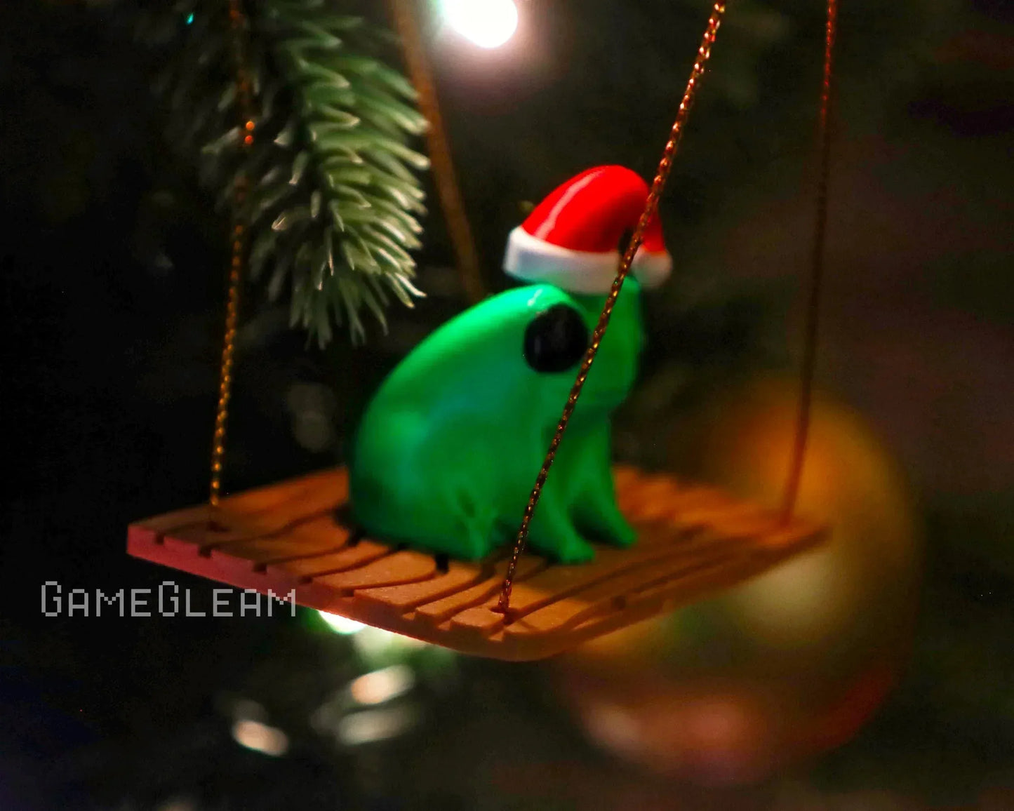 Green frog figurine with Santa hat sitting on a wooden swing Christmas tree ornament.