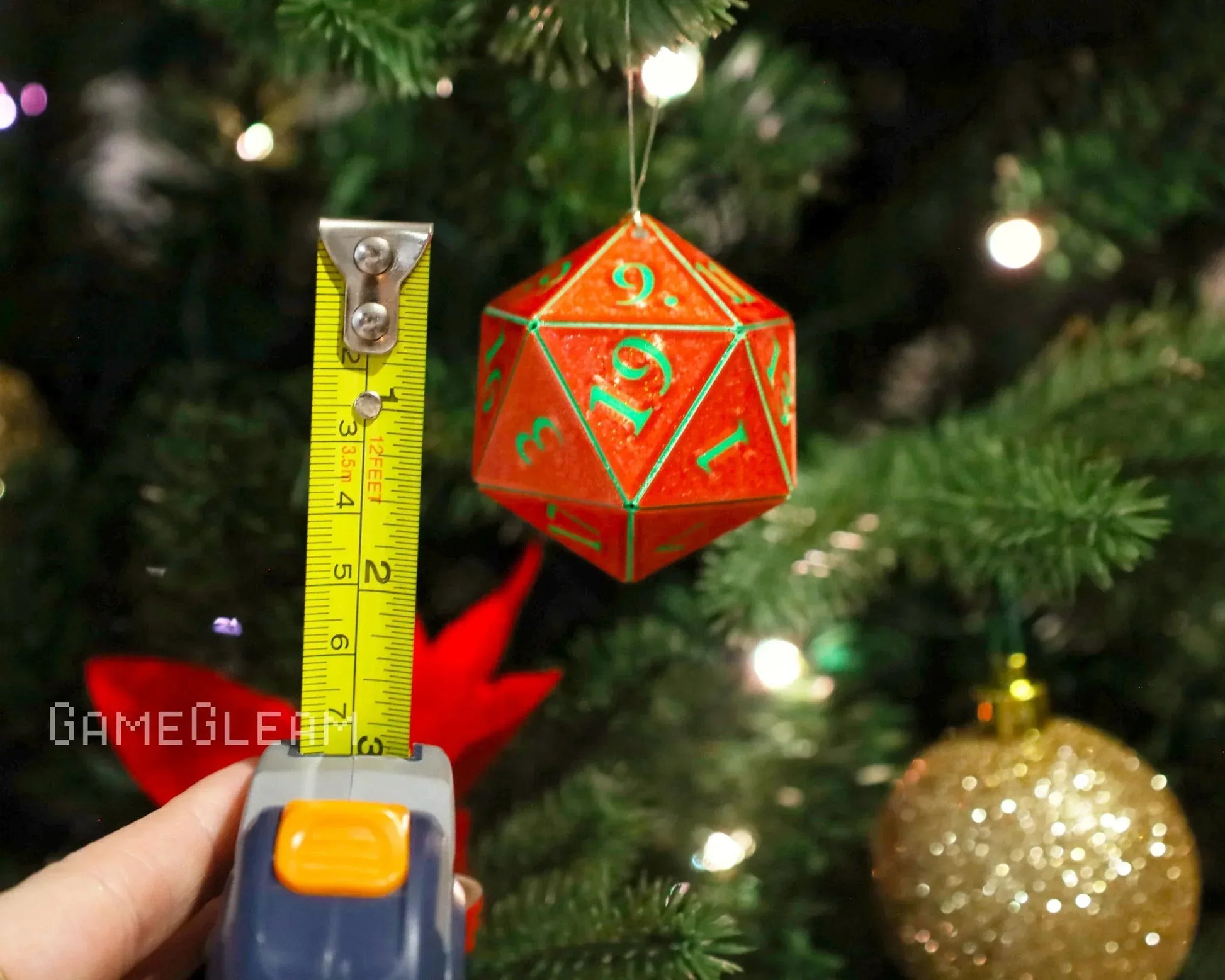 Red 20-sided dice ornament with green numbers hanging on a Christmas tree, tape measure beside it.