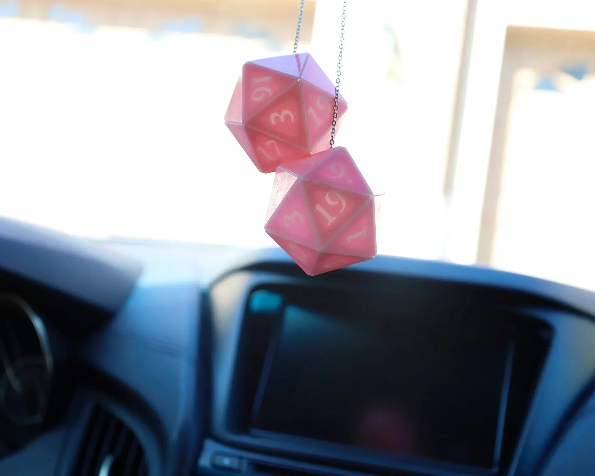 Pink twenty-sided dice car charm hanging from rearview mirror in vehicle interior