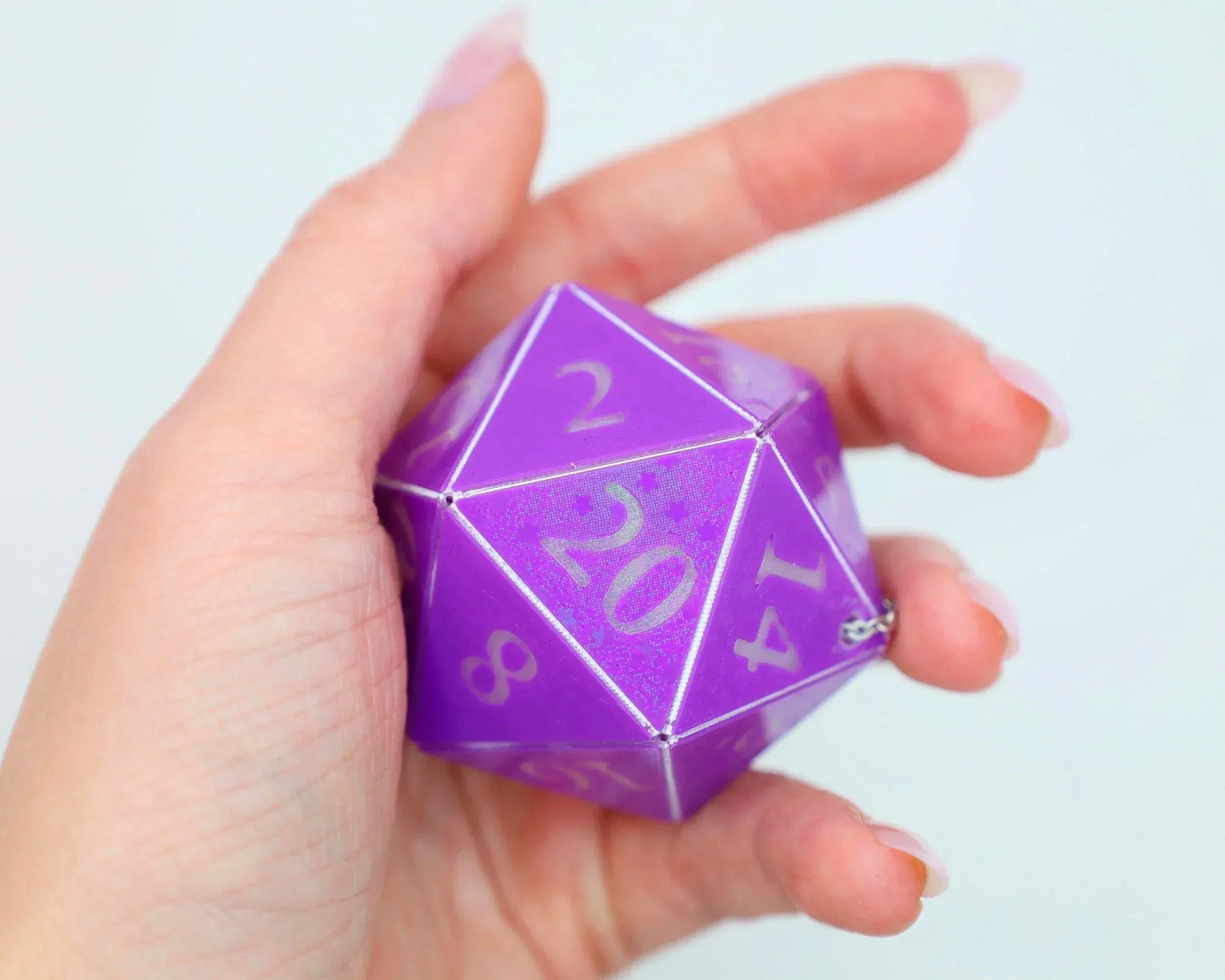 Hand holding large purple 20-sided dice charm with silver numbers for tabletop gamers