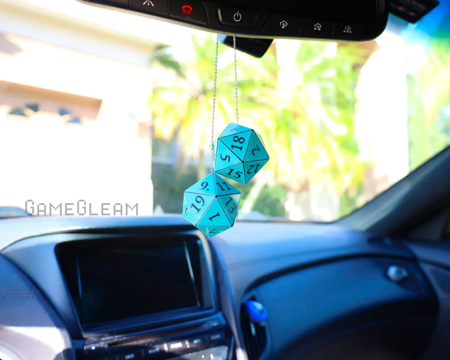 Blue twenty-sided dice car charm hanging from rearview mirror in a sunny car interior