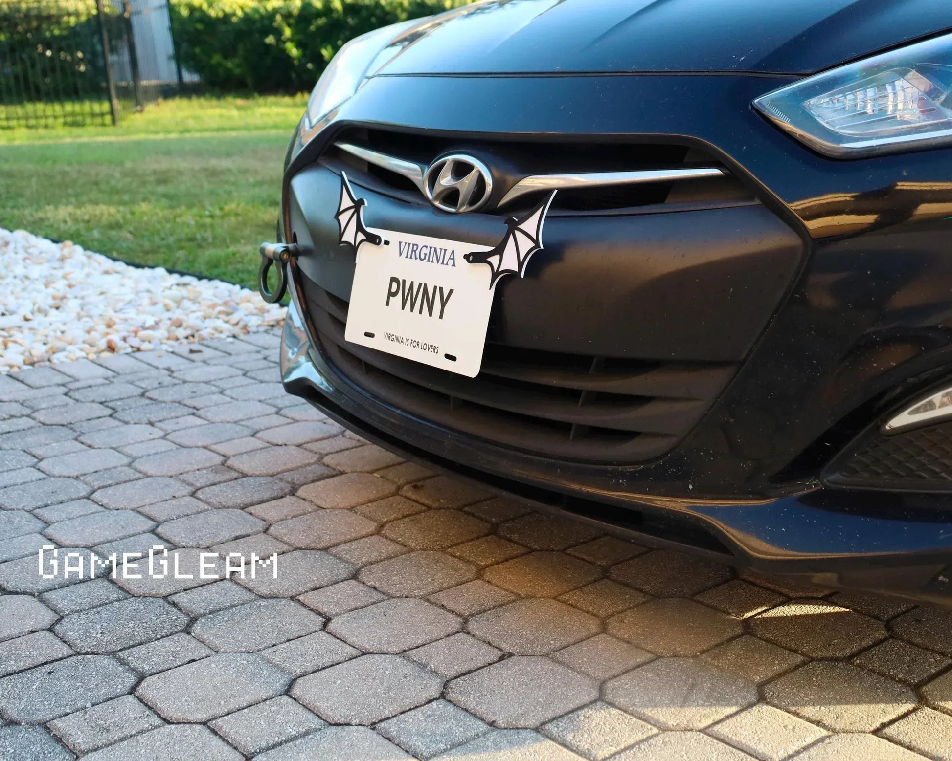 Closeup of a black Hyundai car with a custom license plate frame featuring bat wing accents.