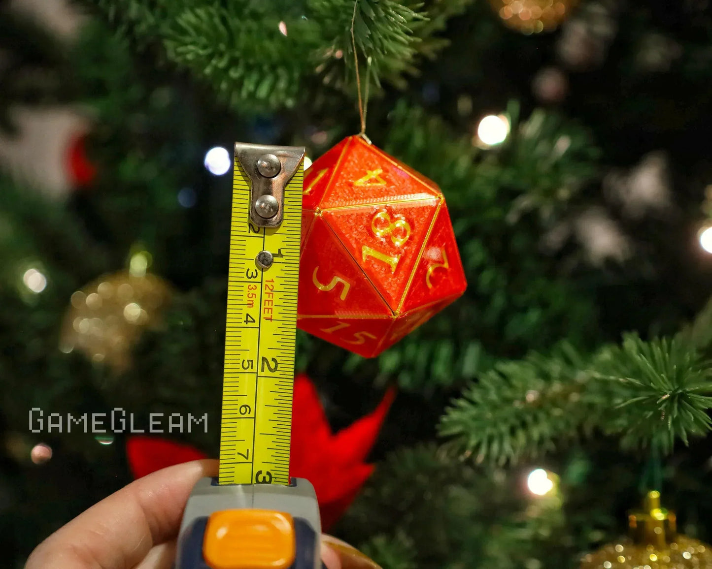 Red twenty-sided dice ornament with yellow numbers on Christmas tree, tape measure for scale