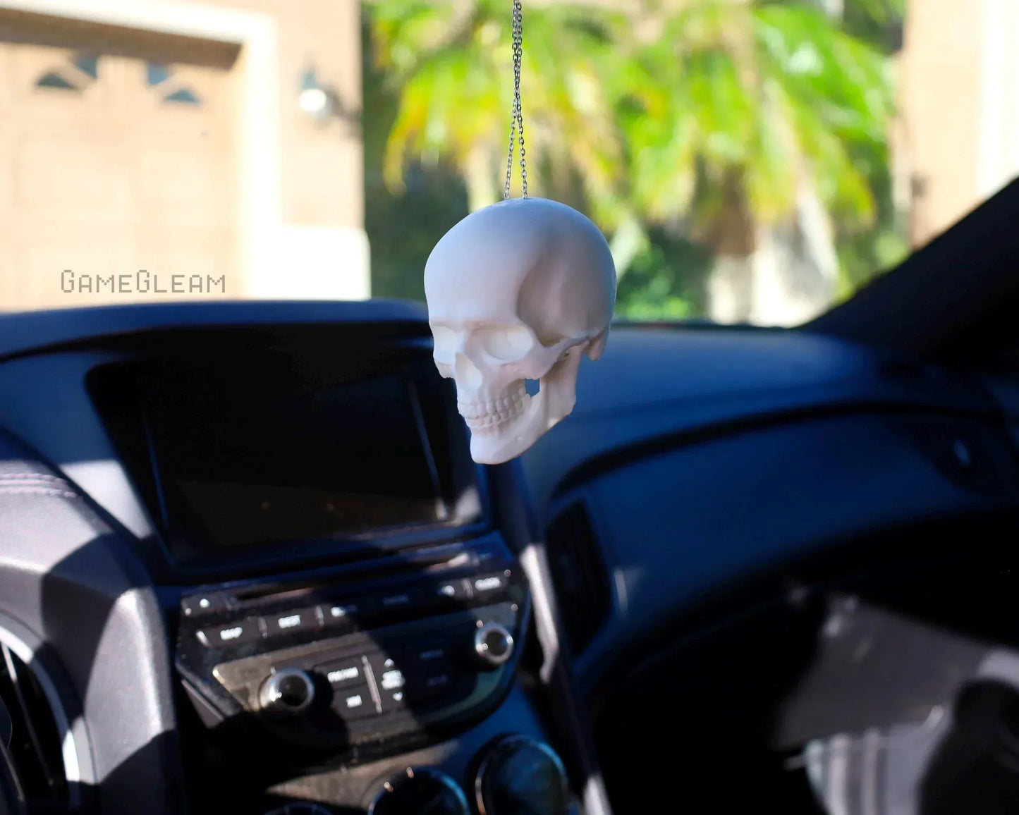 White skull car charm hanging from rearview mirror in a sunlit car interior.