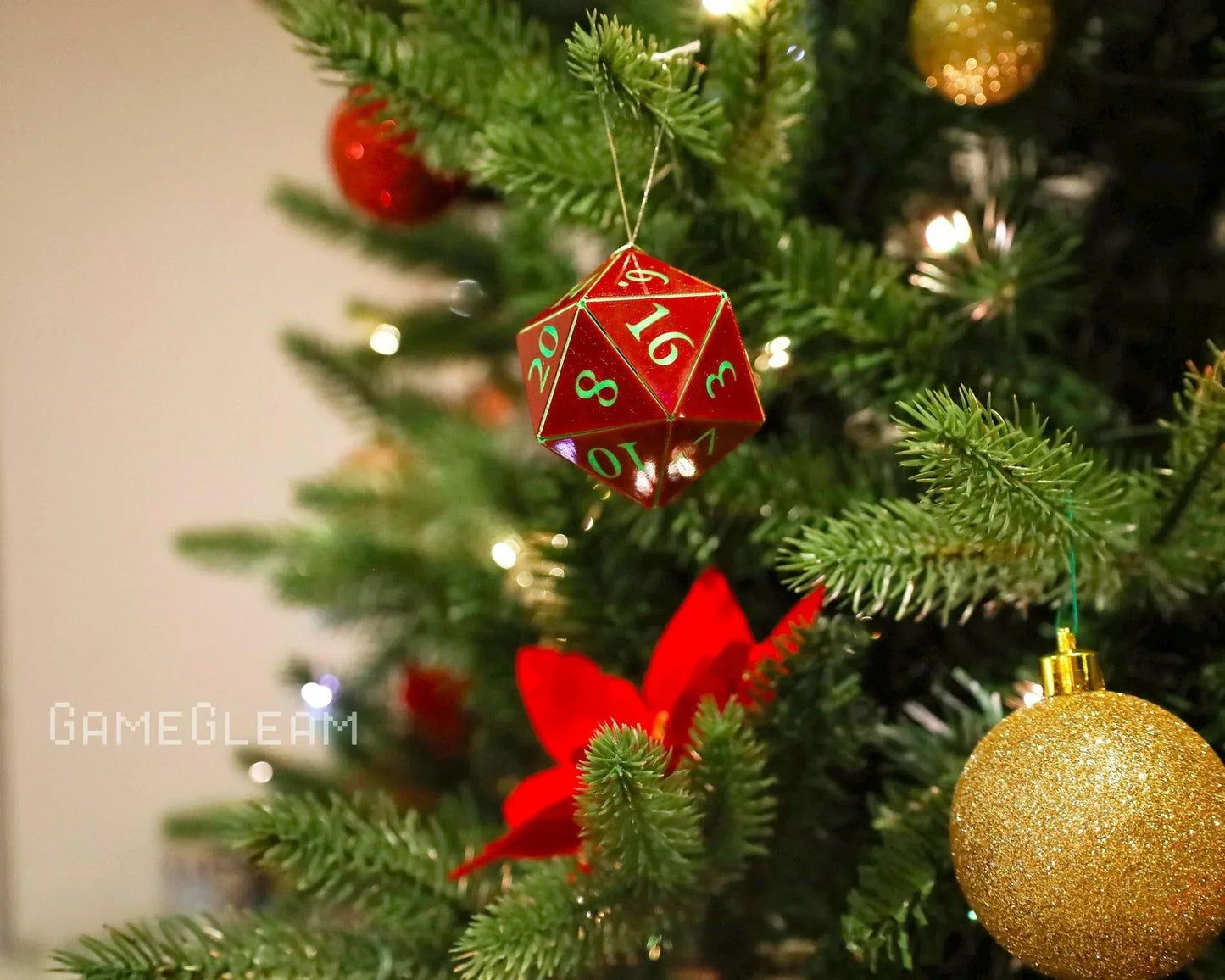 Red 20-sided dice ornament hanging on a lit Christmas tree with gold and red decorations