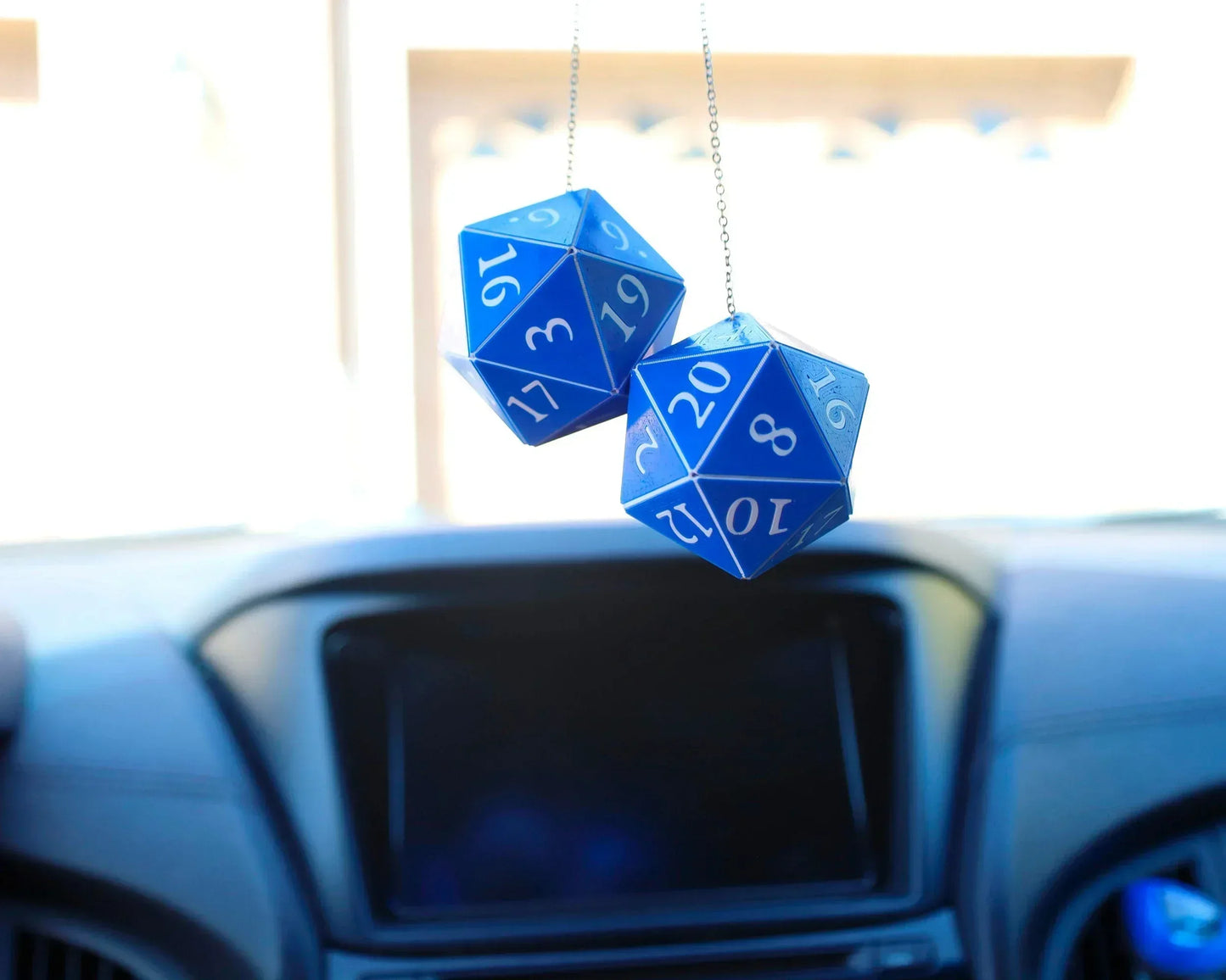 Blue twenty-sided dice car charms hanging from rearview mirror inside a vehicle