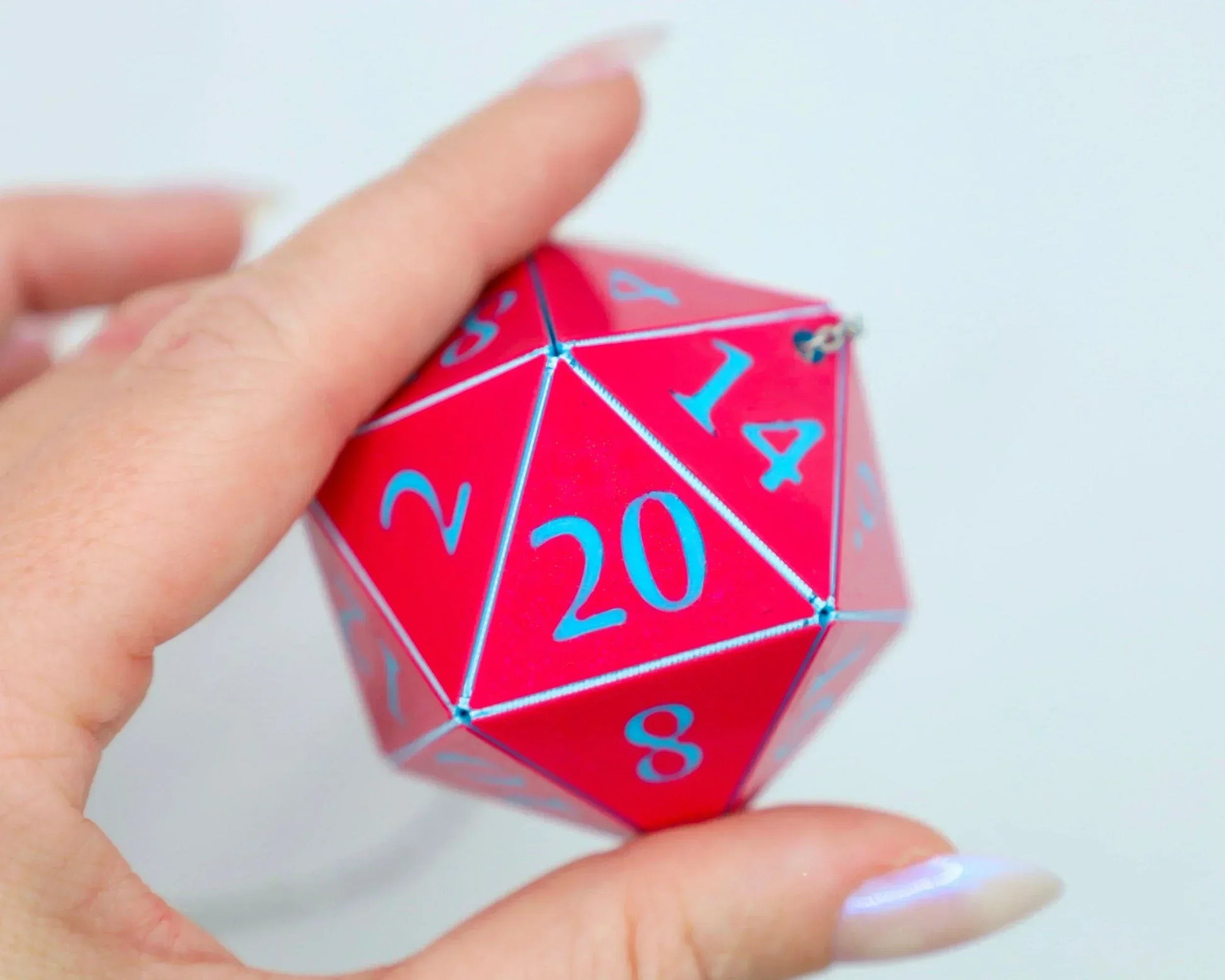 Hand holding a large red twenty-sided dice with blue numbers, gamer car accessory