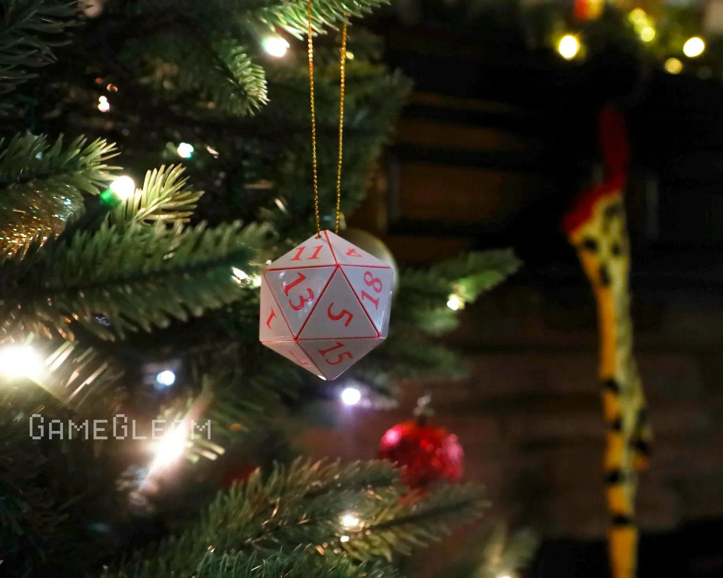 Hanging white polyhedral dice ornament with red numbers on a lit Christmas tree branch.