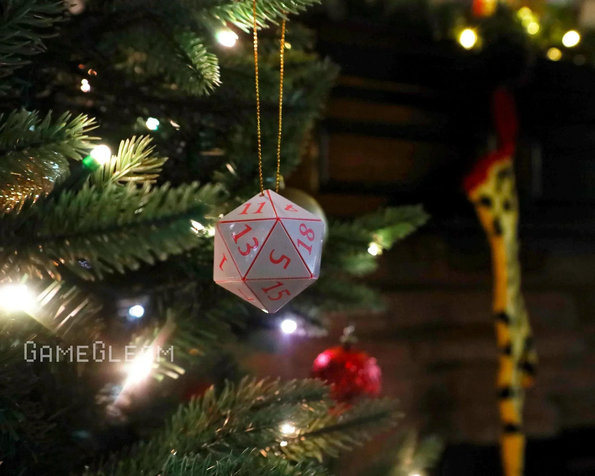 Hanging white polyhedral dice ornament with red numbers on a lit Christmas tree branch.