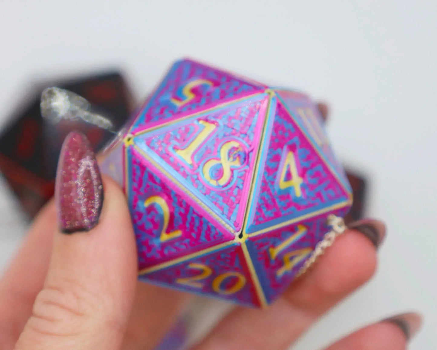 Hand holding a vibrant holographic D20 dice charm with gold numbers, gamer gift accessory