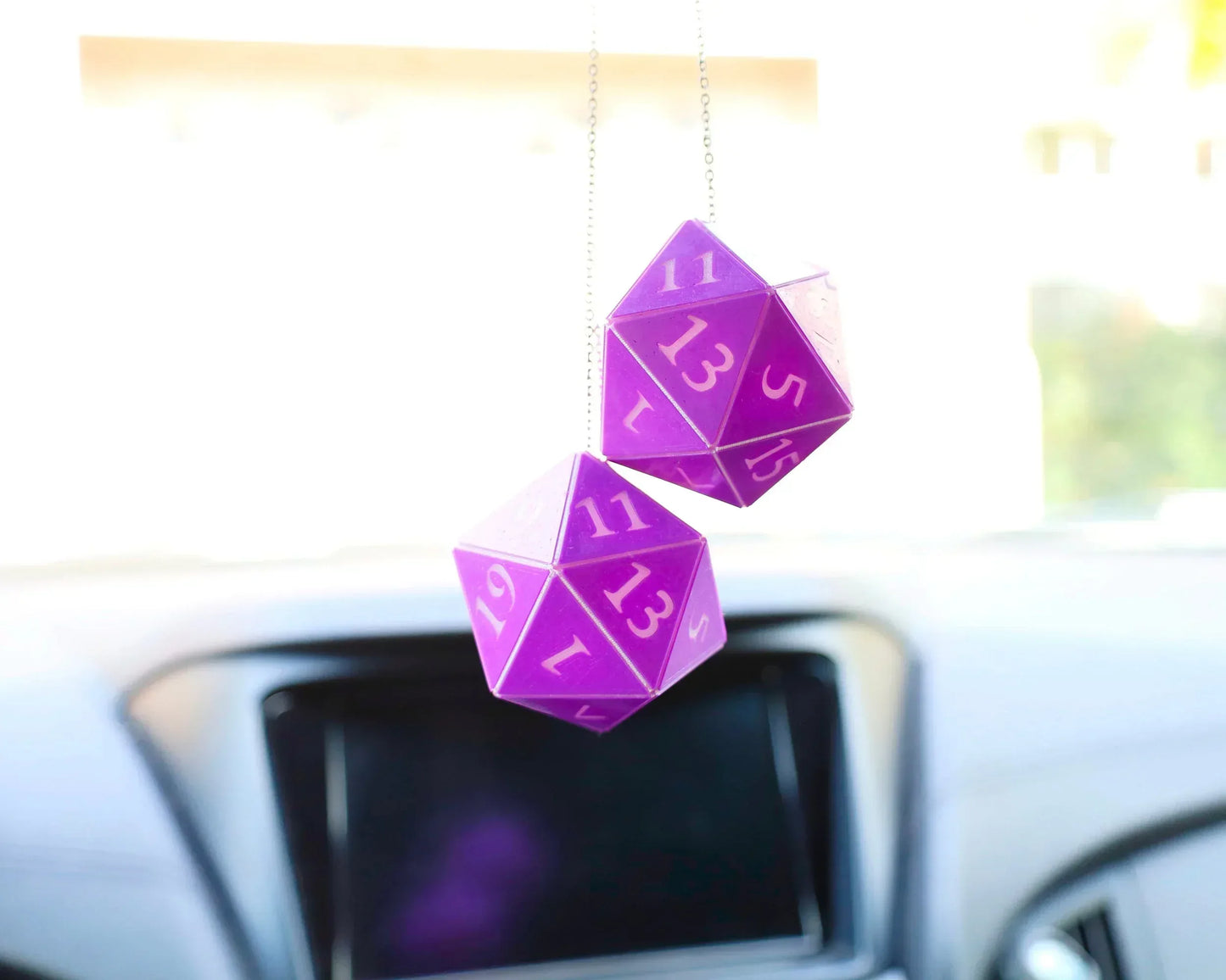 Purple twenty-sided dice car charm hanging on rearview mirror inside a vehicle