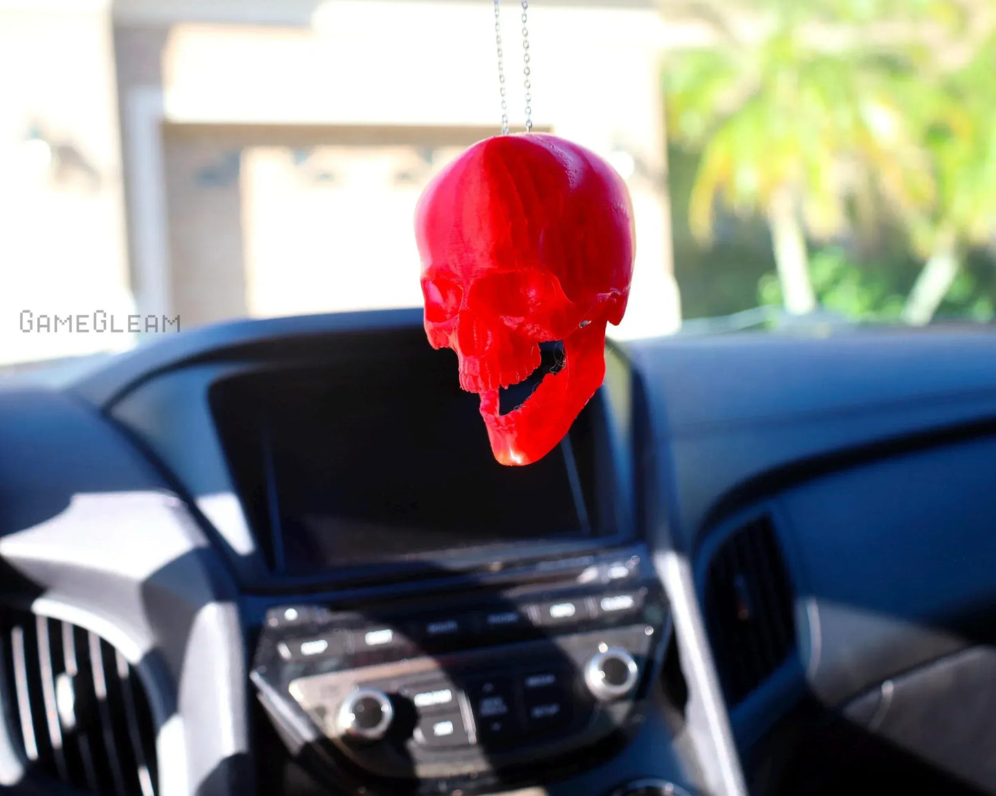 Red skull car charm hanging from rearview mirror in modern car interior, sunlight background