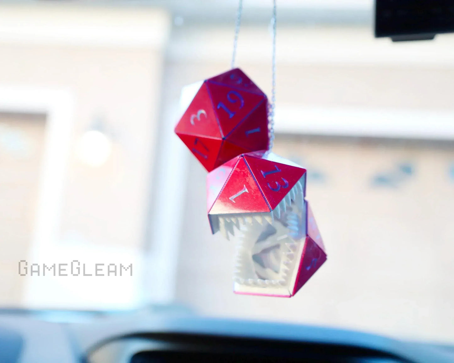 Red holographic twenty-sided dice car charm with a geometric monster design hanging from a rearview mirror.