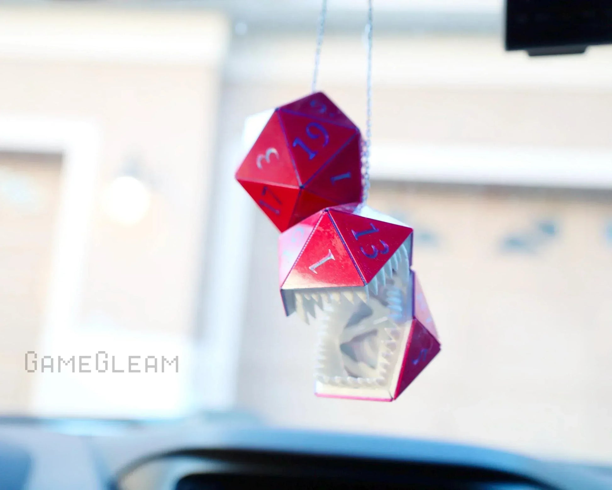 Red holographic twenty-sided dice car charm with a geometric monster design hanging from a rearview mirror.