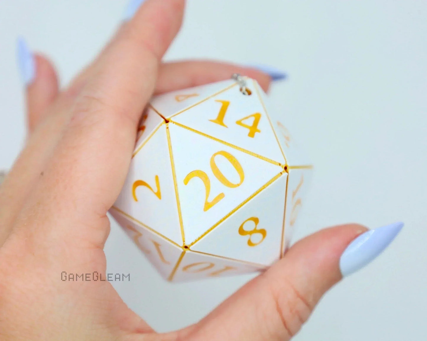 Hand holding a white and gold 20-sided dice car accessory with large numbers and keychain loop.