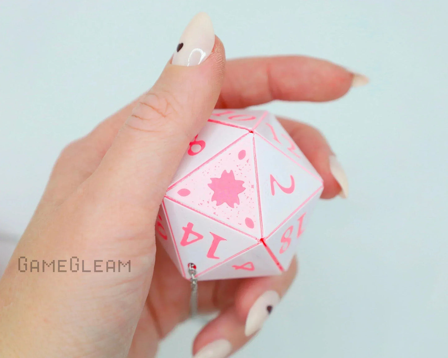 Hand holding a pink and white twenty-sided dice car charm with chain attachment