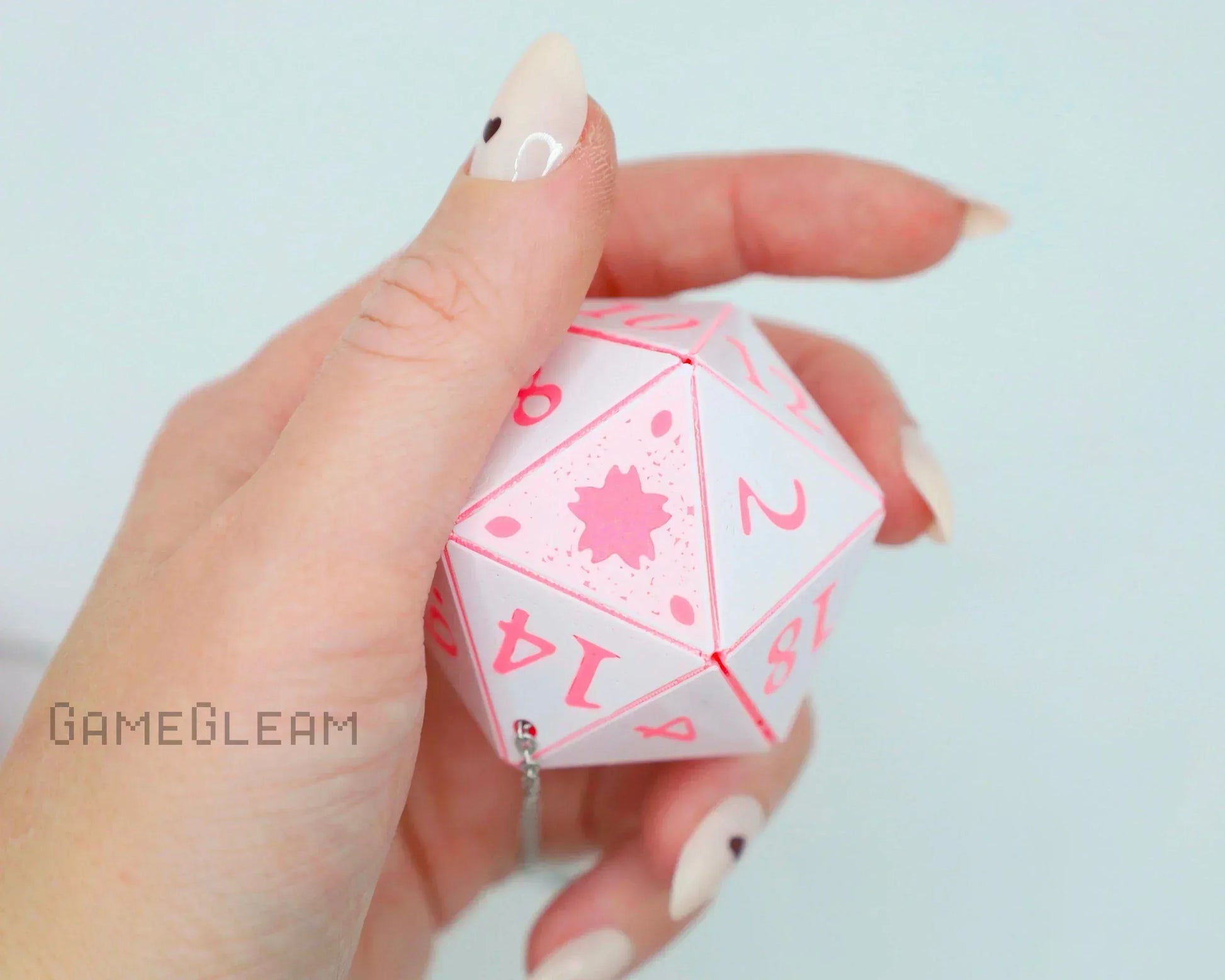 Hand holding a pink and white twenty-sided dice car charm with chain attachment