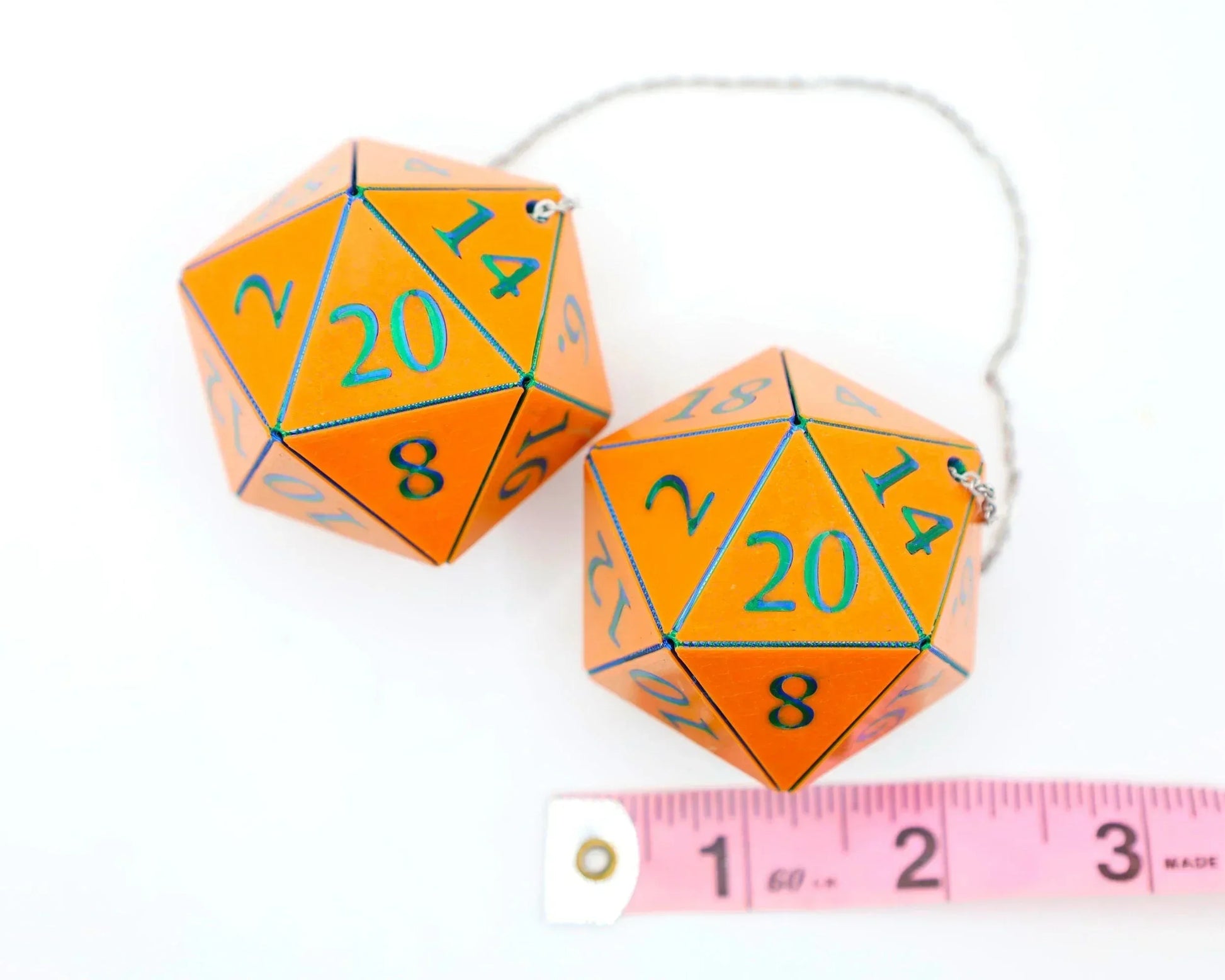 Pair of orange twenty-sided dice car charms with blue numbers, chain attached, next to ruler