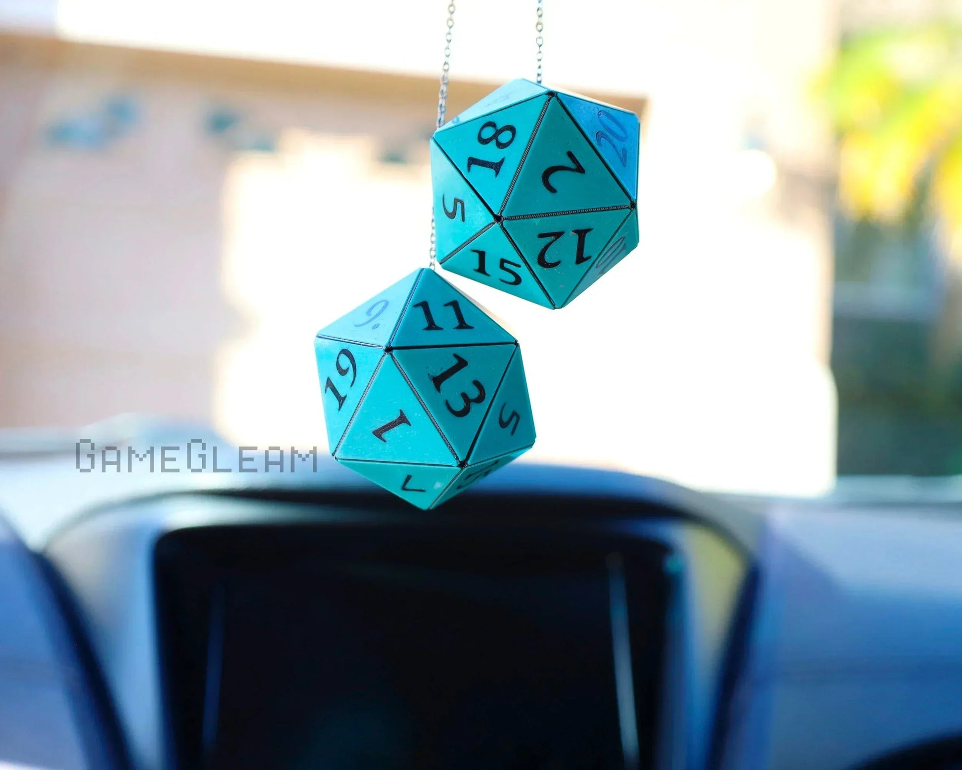 Pair of teal 20-sided dice car charms hanging from a rearview mirror in sunlight