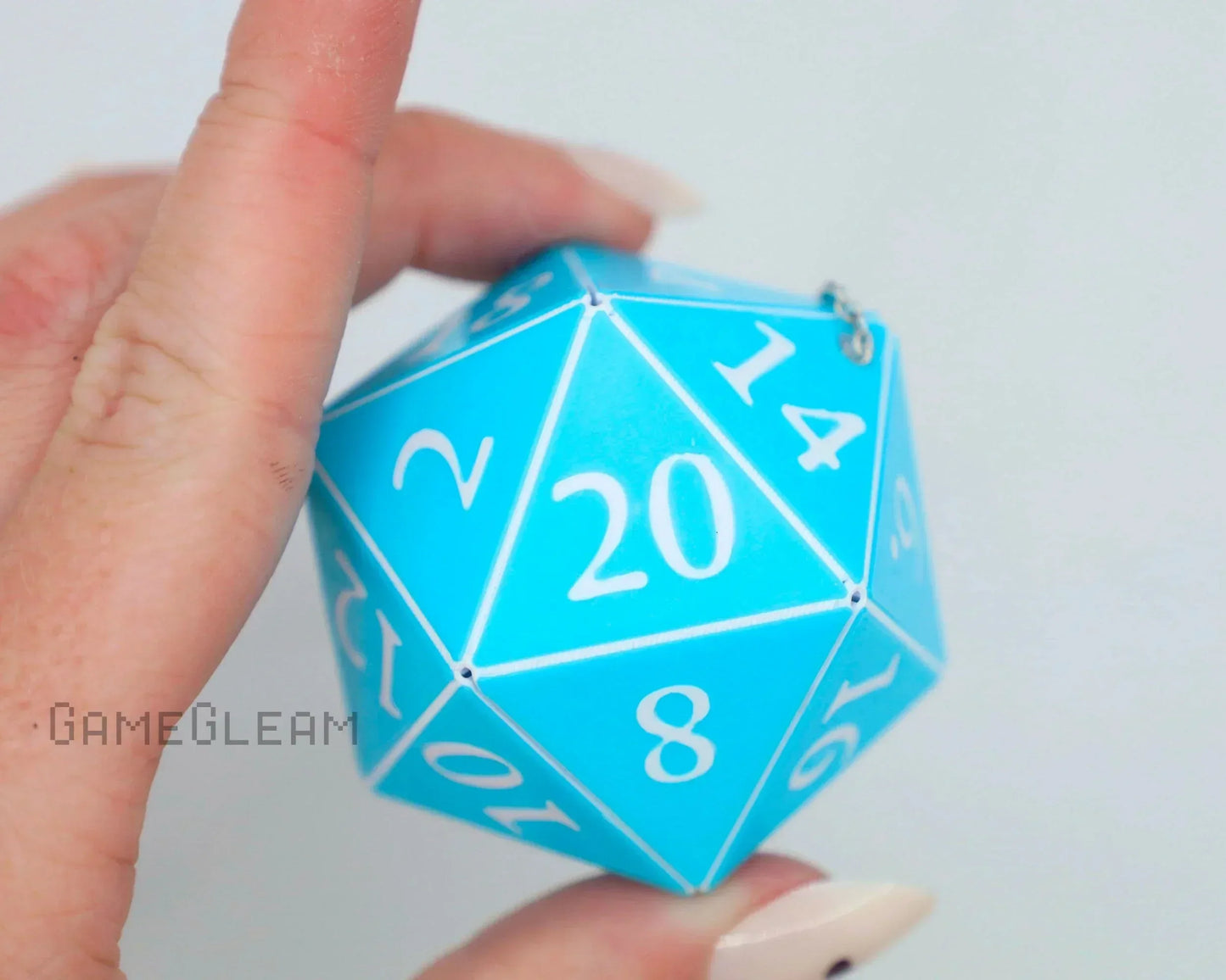 Hand holding a large blue twenty-sided dice charm with white numbers, close-up view.