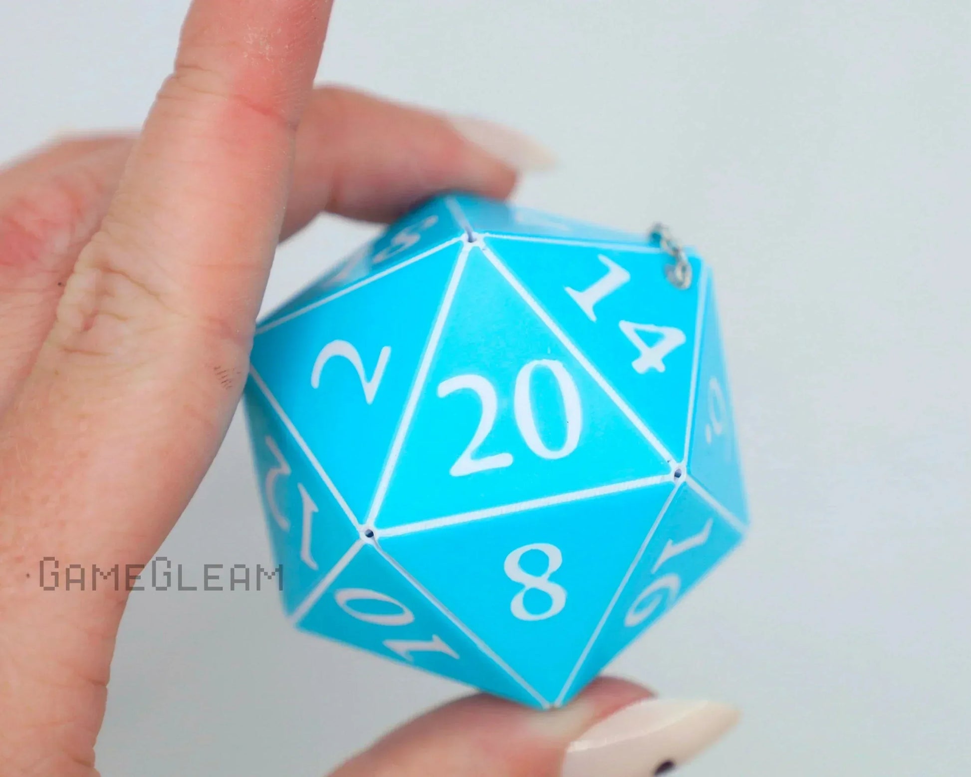 Hand holding a large blue twenty-sided dice charm with white numbers, close-up view.