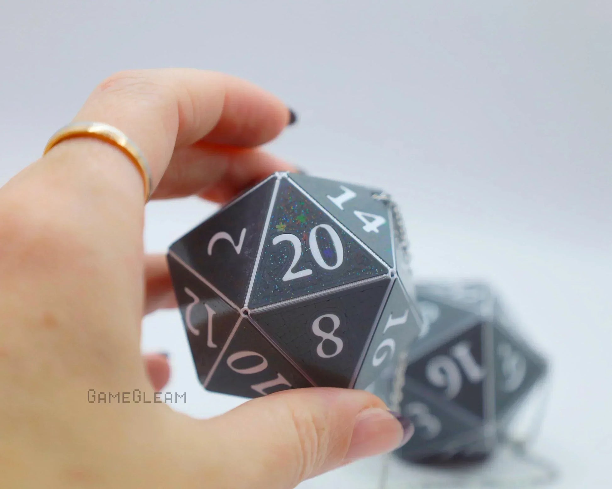 Hand holding a black holographic 20-sided dice car charm with white numbers, geek gift