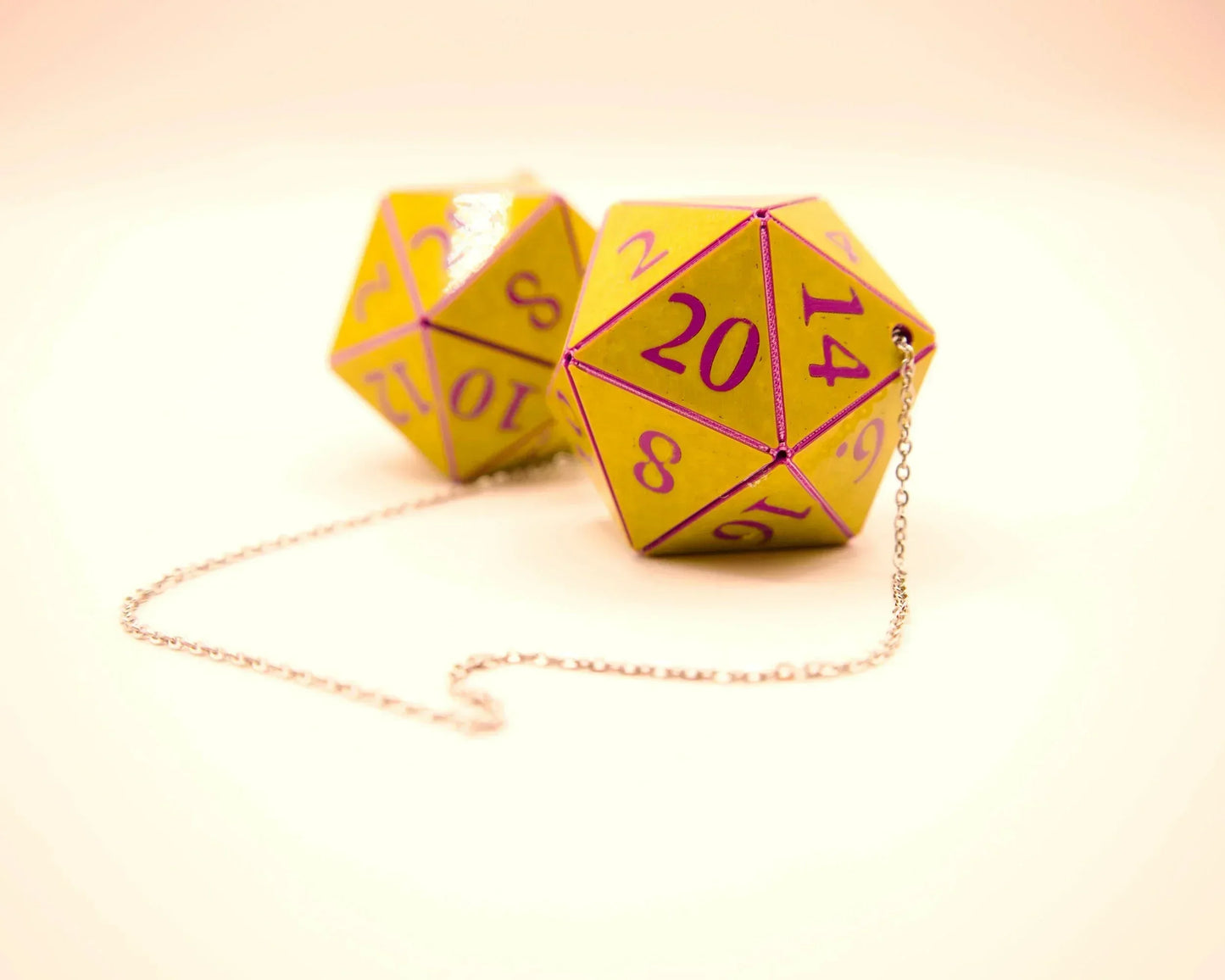 Yellow twenty-sided dice car charm with purple numbers and a silver chain on a light background