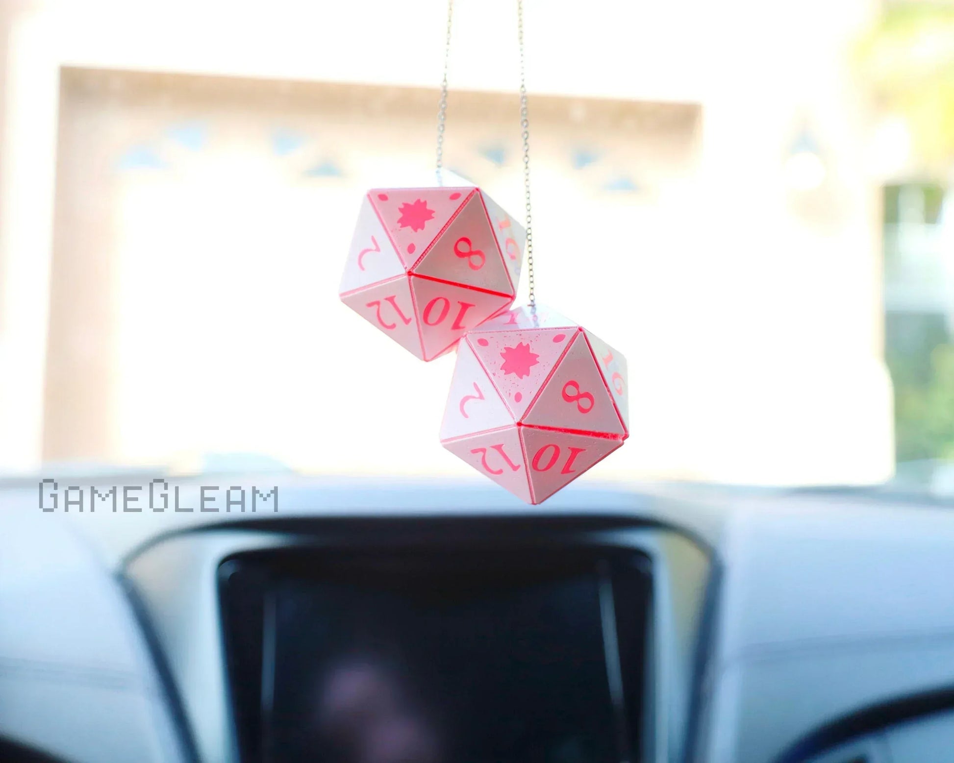Pink handmade twenty-sided dice car charms hanging from a rearview mirror inside a vehicle