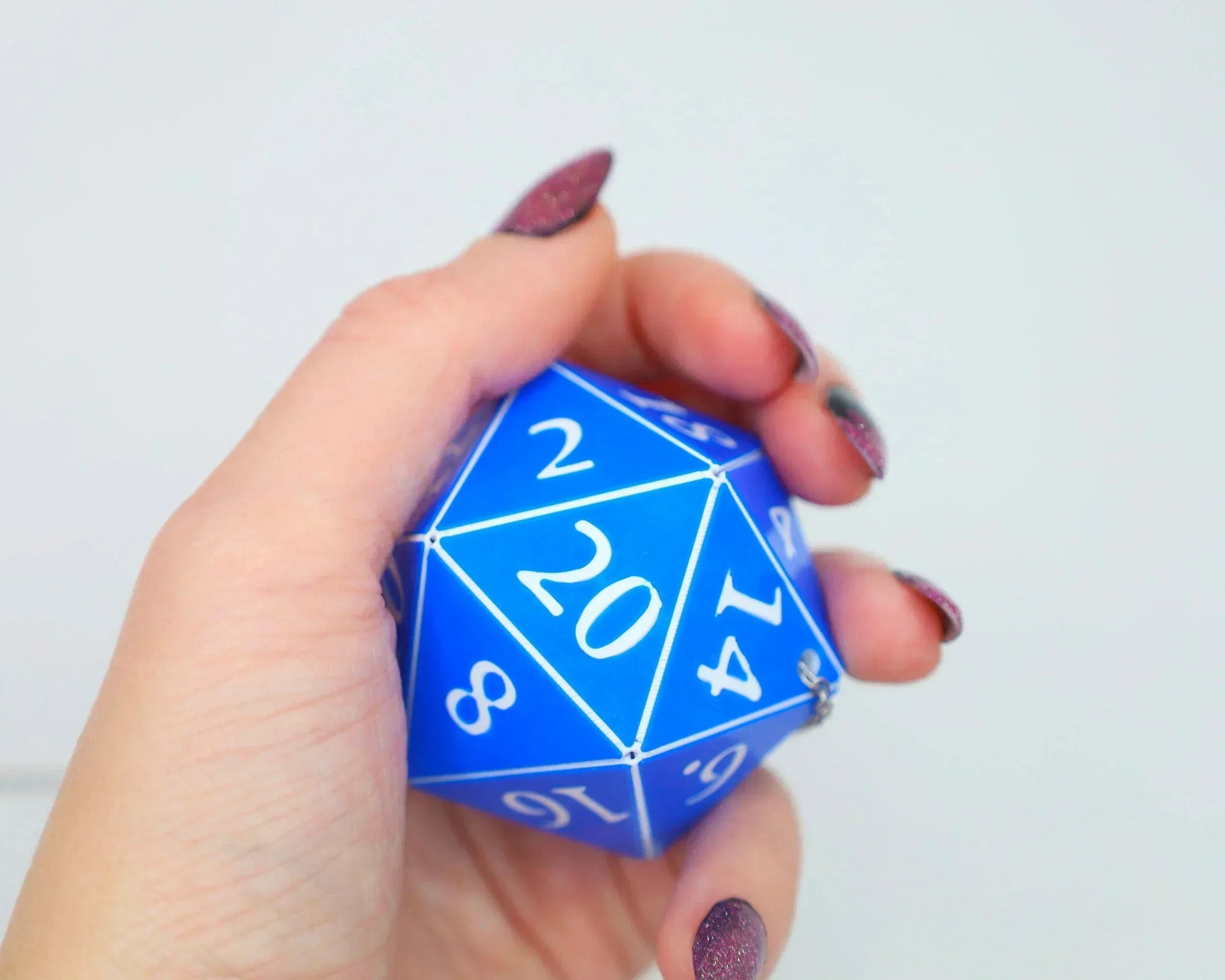 Hand holding a large blue twenty-sided dice charm with white numbers, ideal gamer gift
