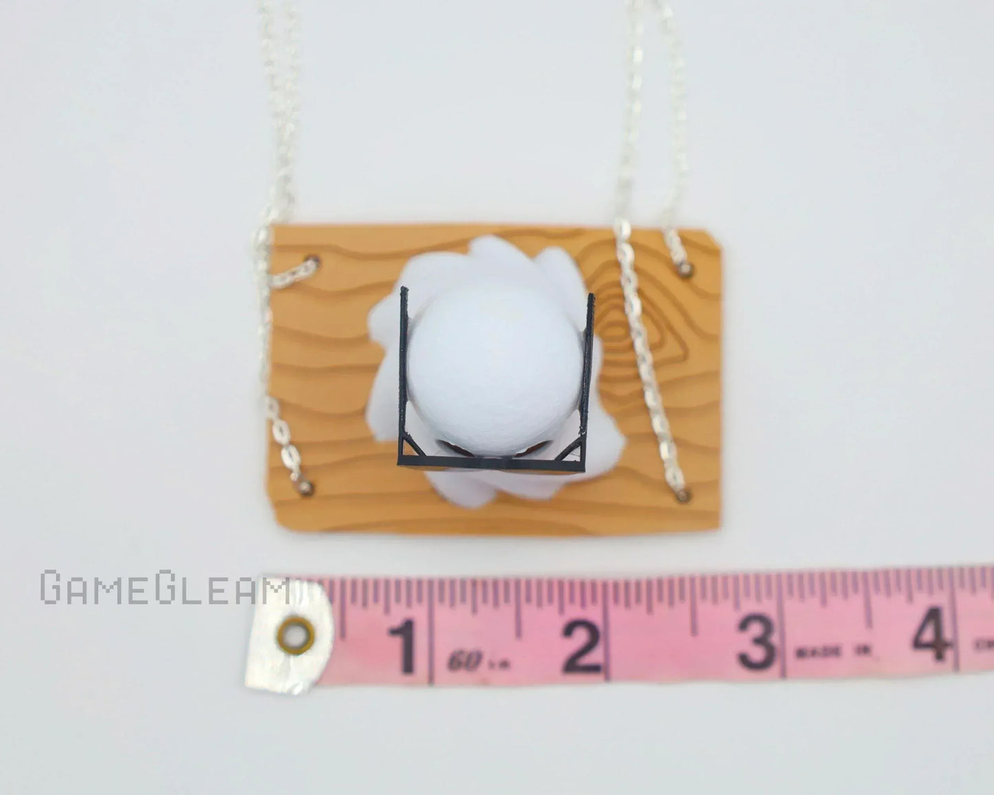 Miniature handmade white spell effect pendant with wood-look base and chain, next to ruler for scale