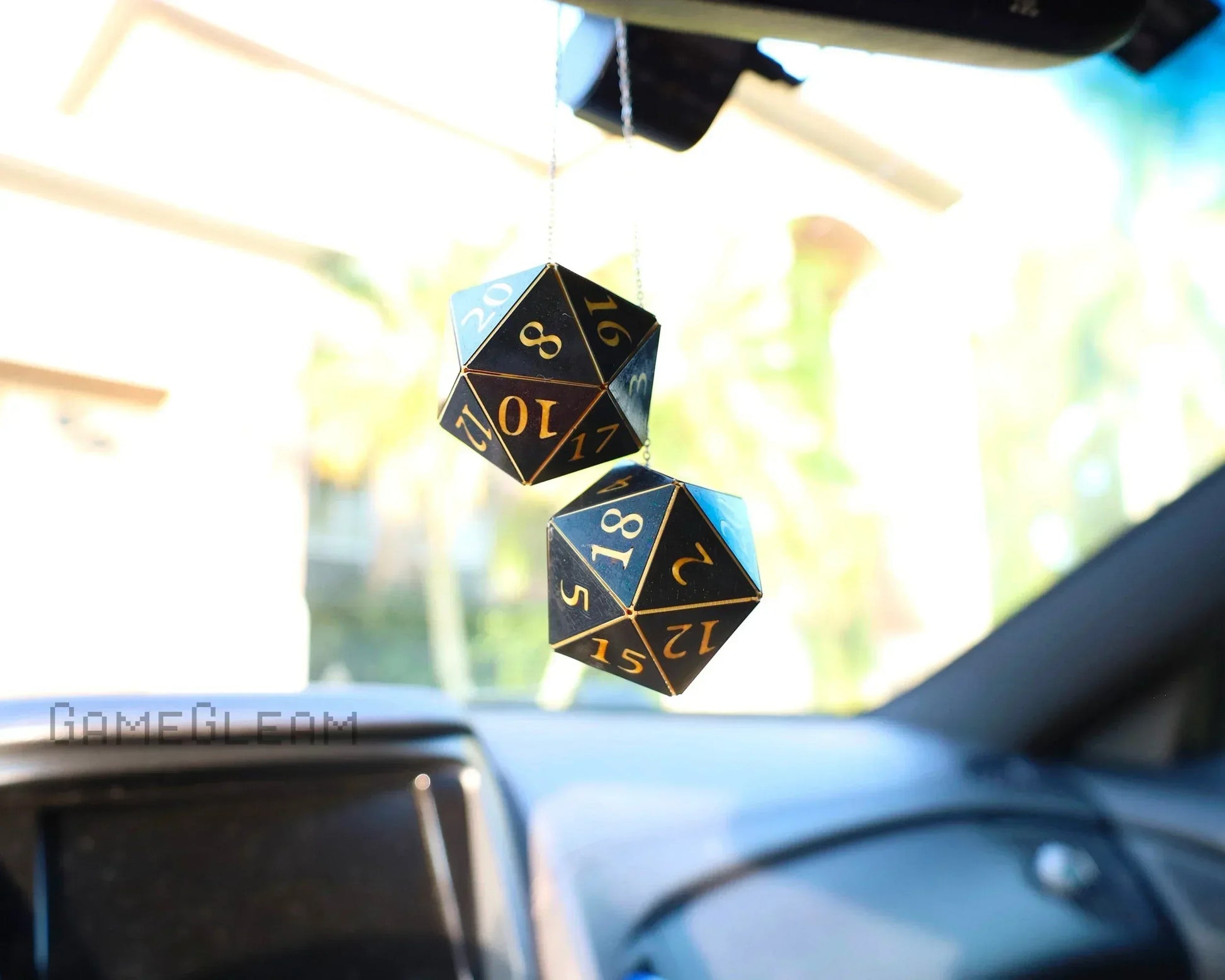 Pair of black and gold twenty-sided dice hanging from a car rearview mirror