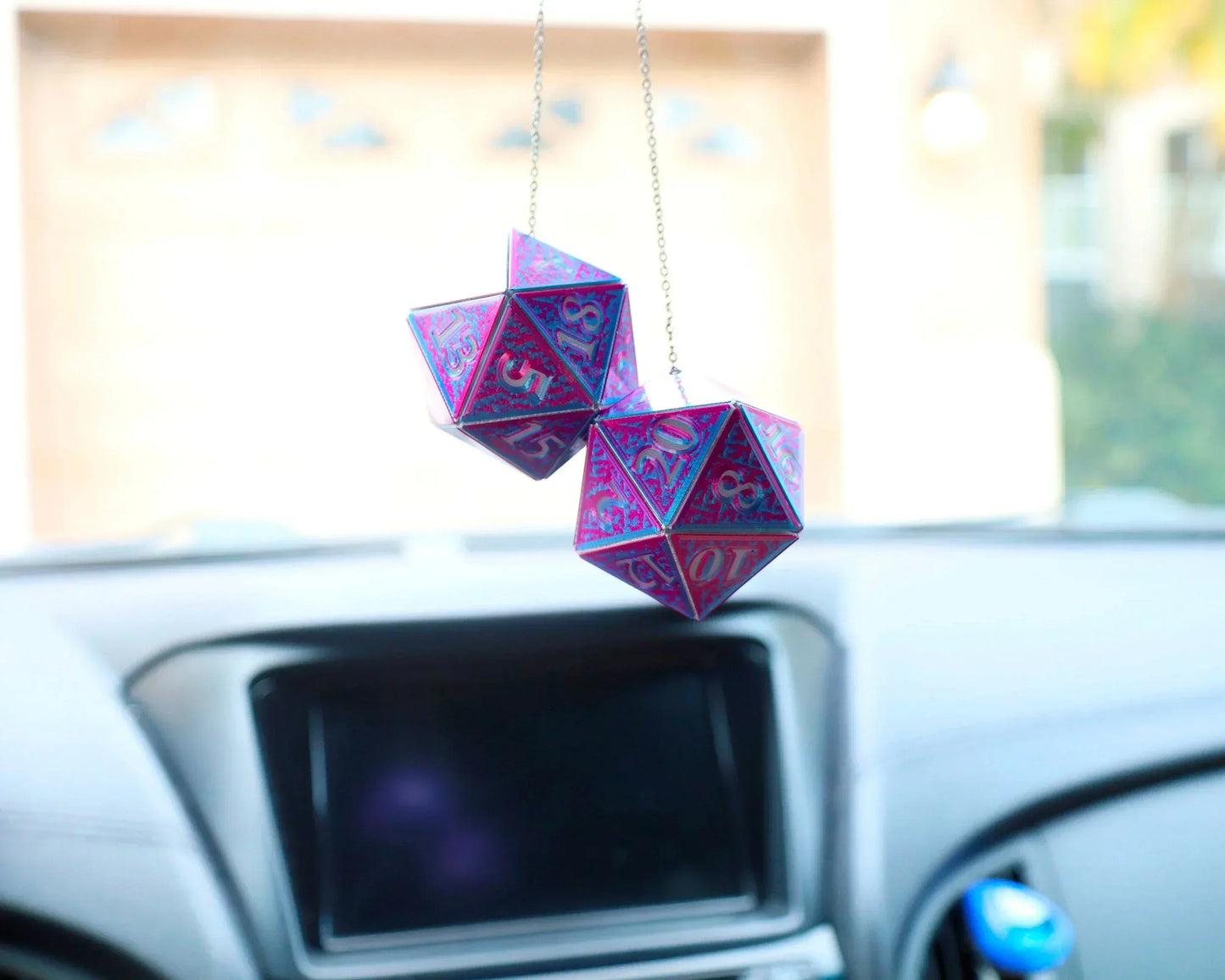 Holographic twenty-sided dice car charm with pink and blue design hanging in a vehicle.