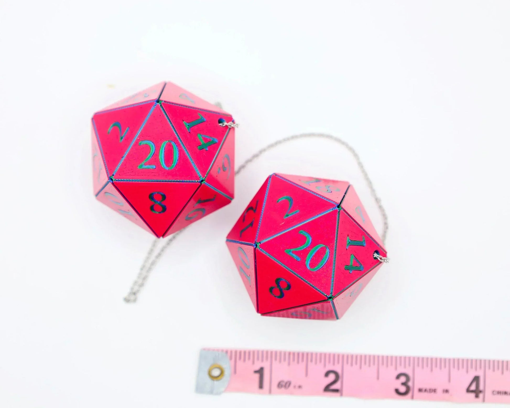 Two red 20-sided dice charms with green numbers on ball chains, next to a measuring tape