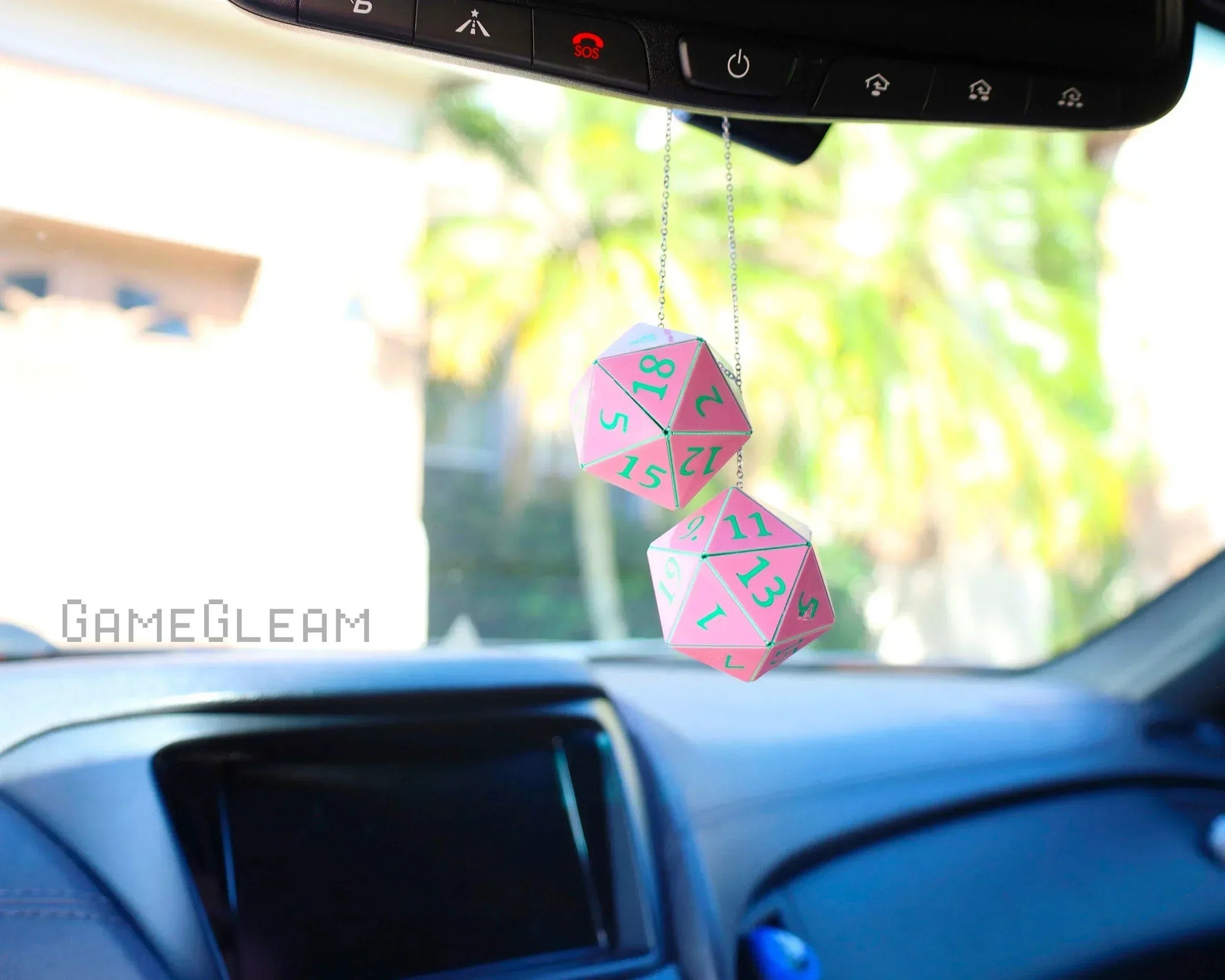Pink 20-sided dice car mirror charm hanging in vehicle interior, sunlight background