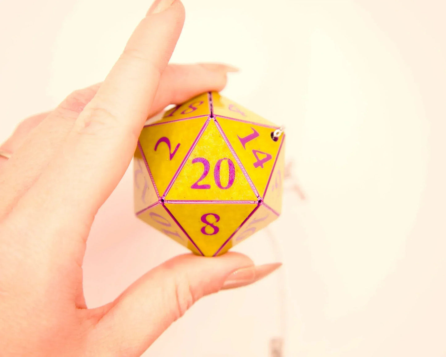 Hand holding a yellow twenty-sided polyhedral dice charm with purple numbers