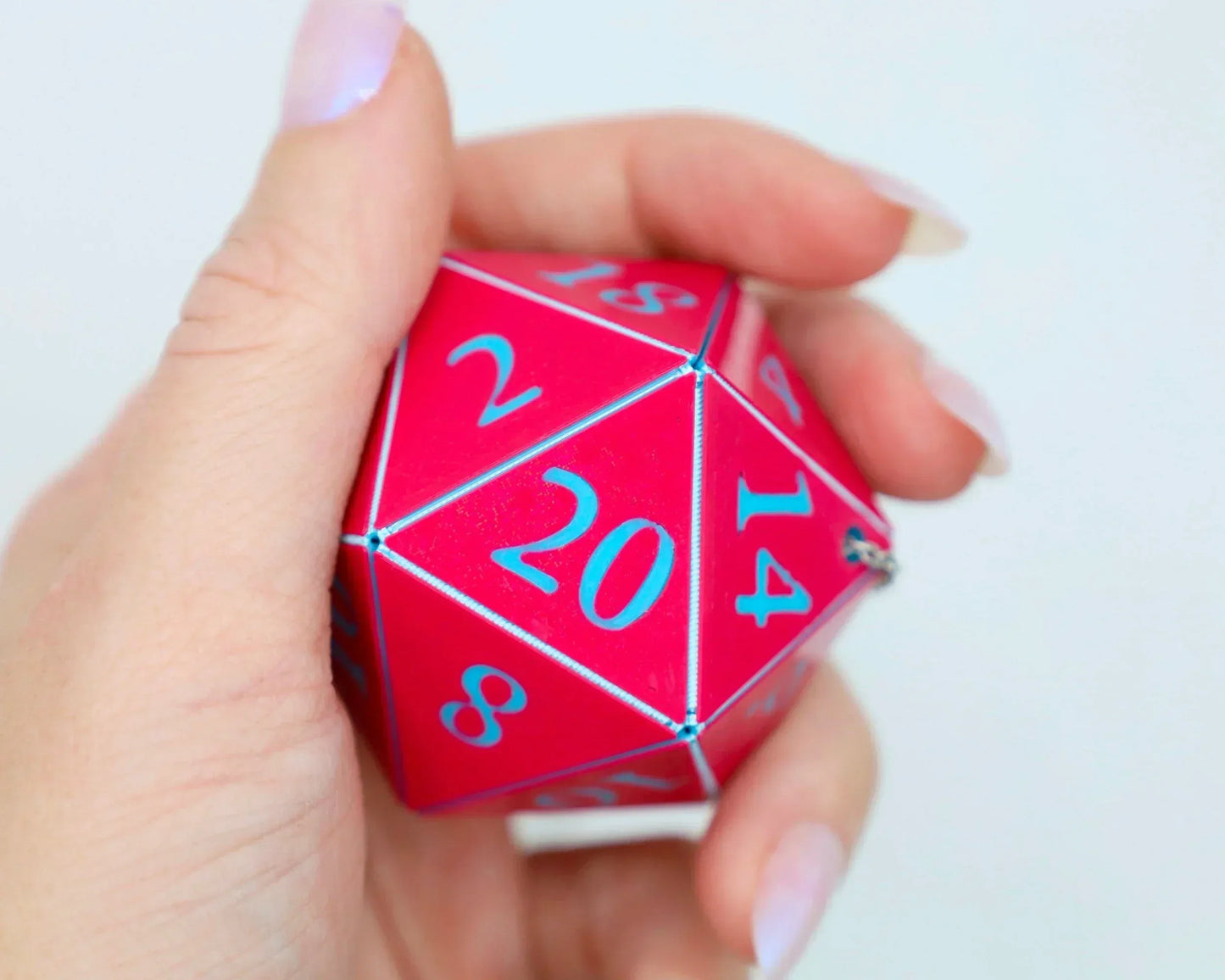 Hand holding a large red twenty-sided dice with blue numbers, tabletop RPG accessory.